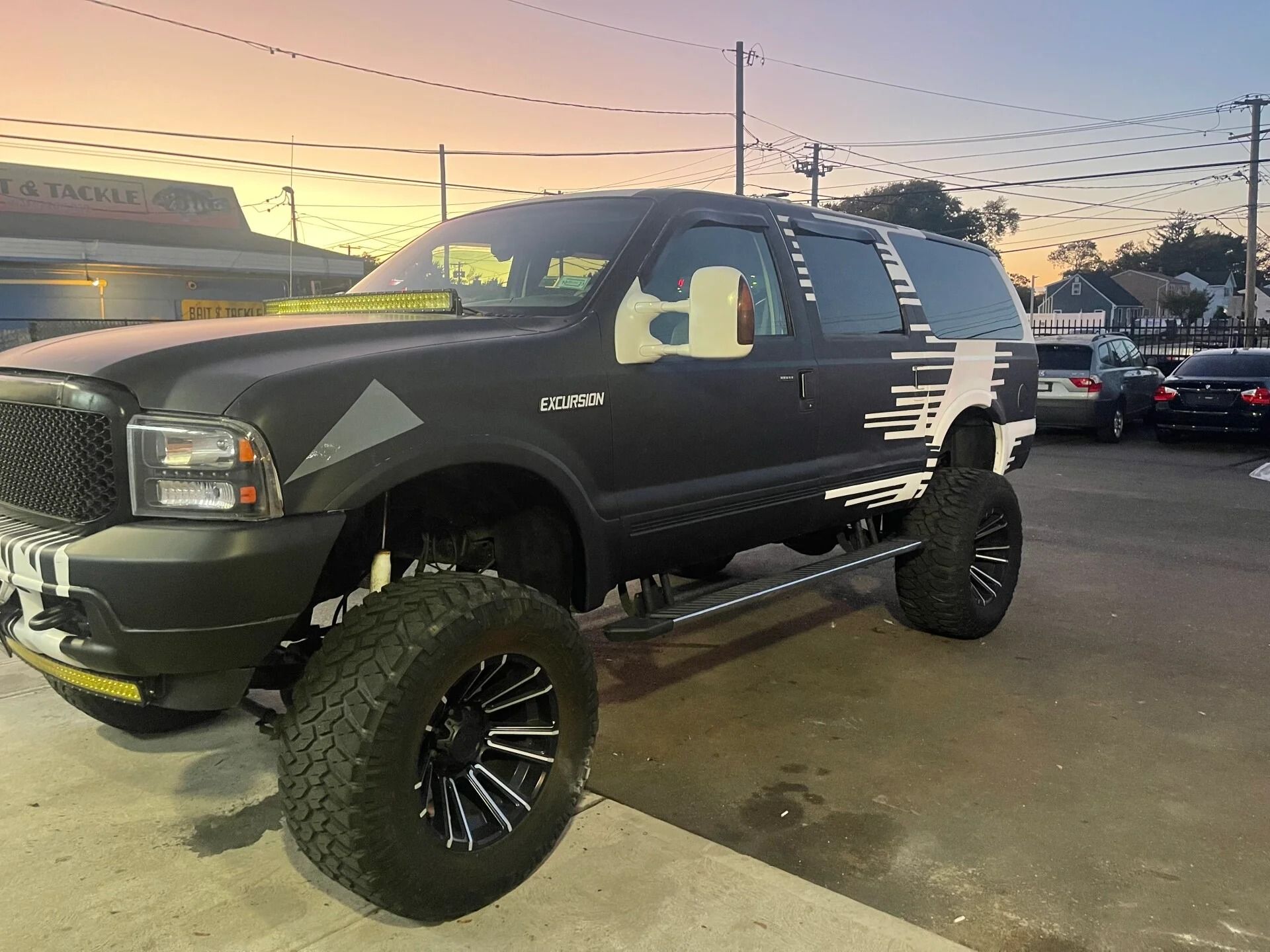 Lifted black pickup truck with oversized tires parked at dusk in a lot.