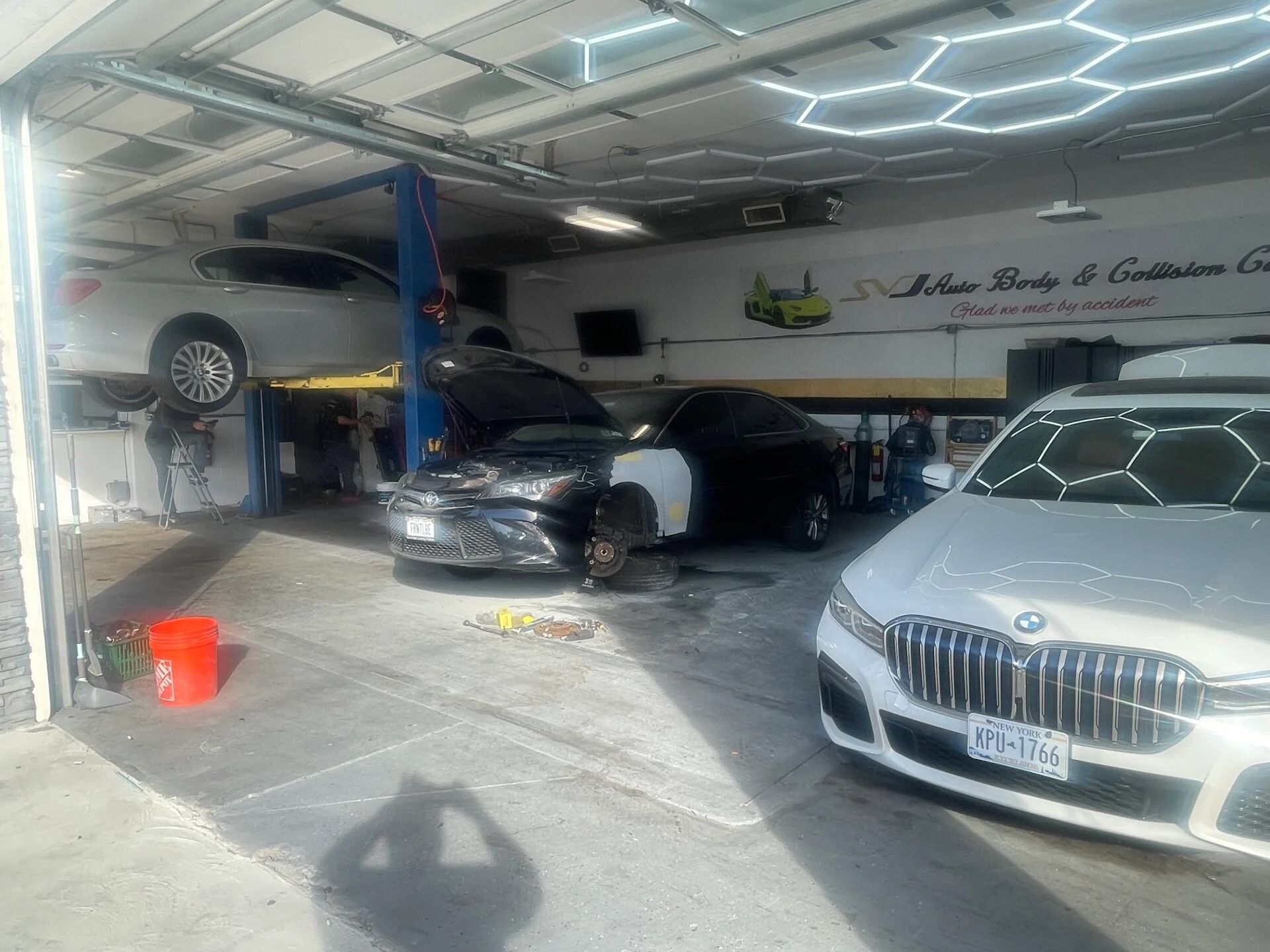 Car showroom with three cars, including a silver BMW in front and a black car on a lift.