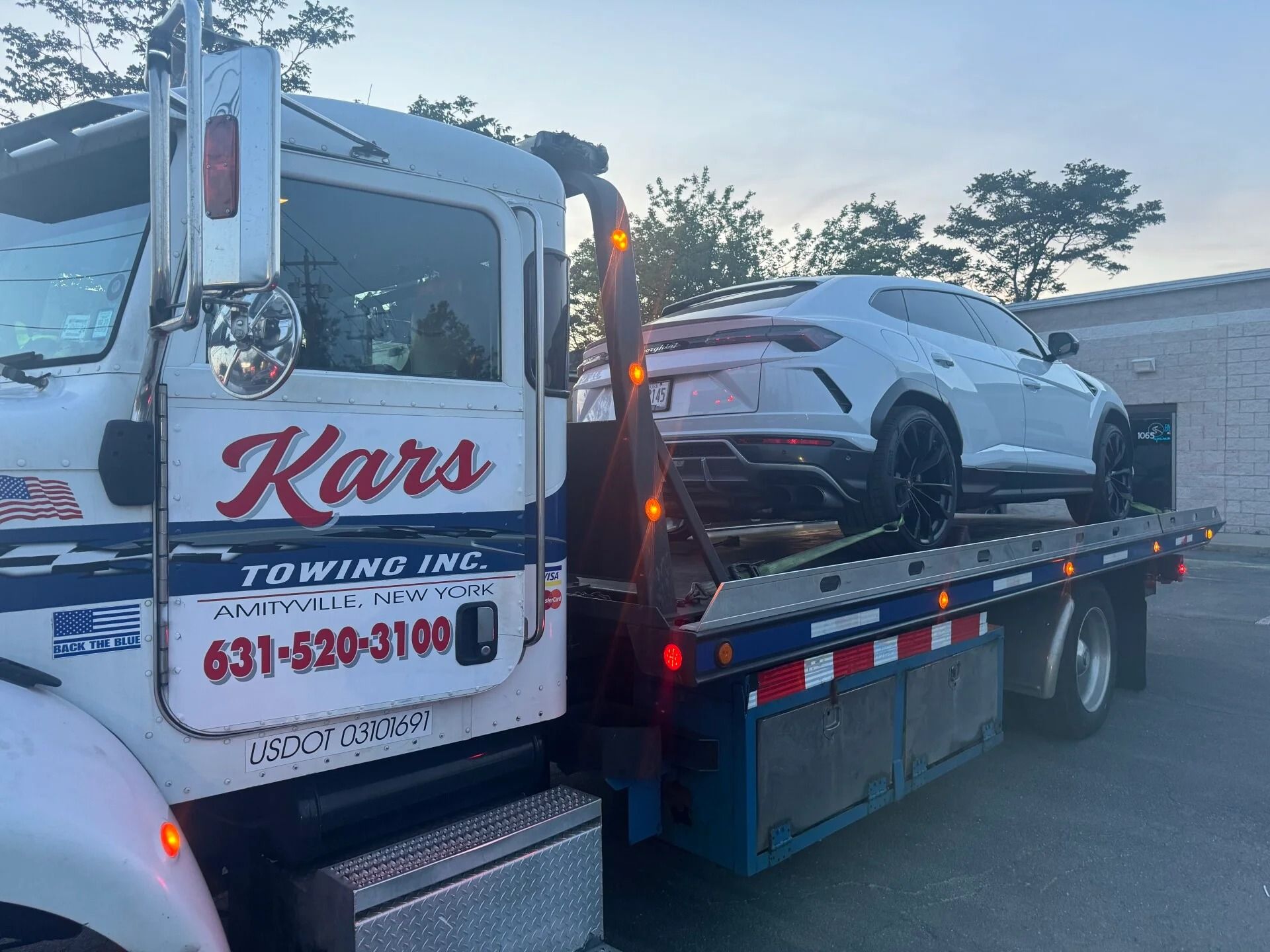 Tow truck hauling a white SUV on a flatbed at dusk, with “Karl’s Towing” on the cab.