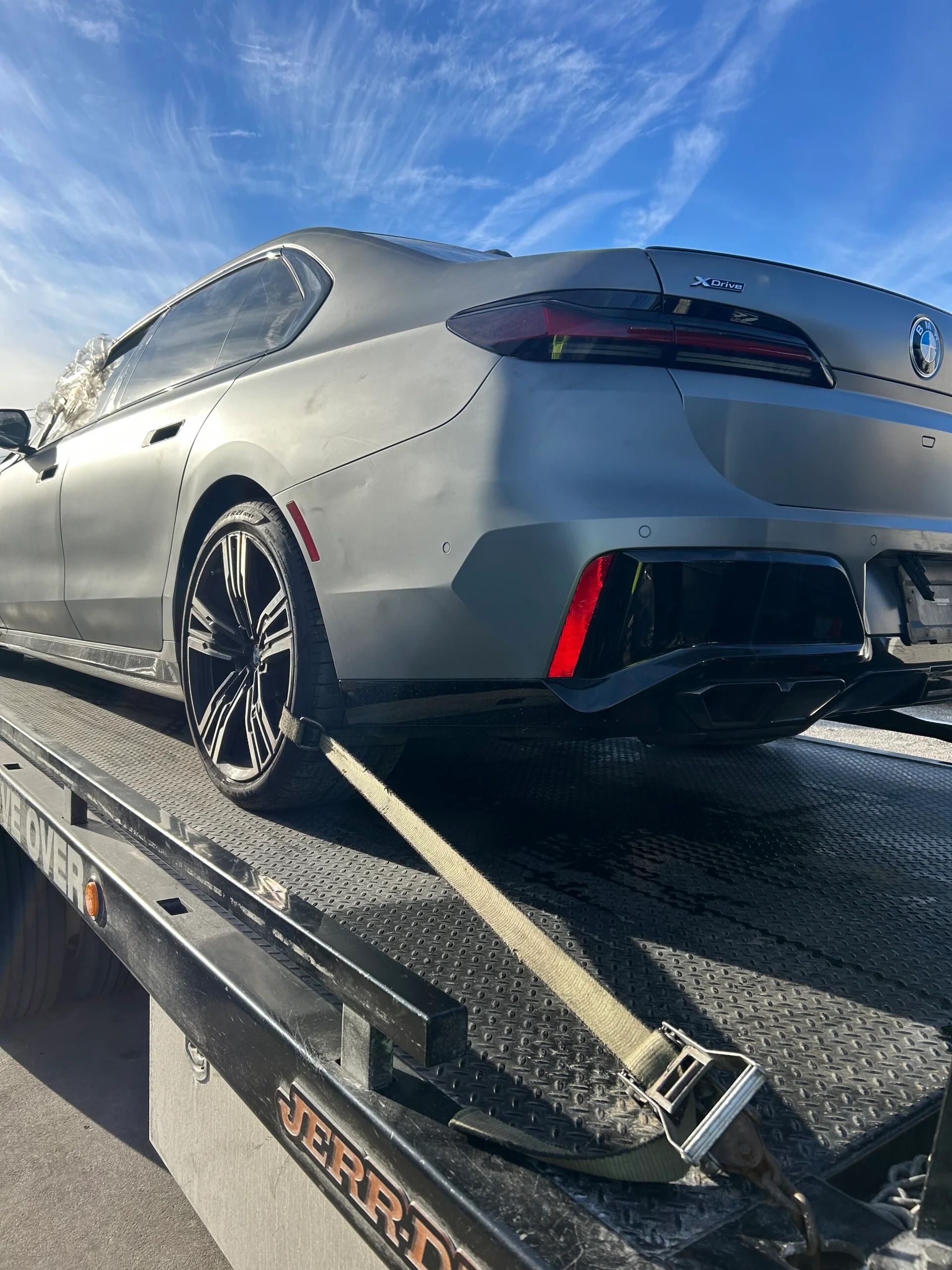 Silver sports car on a tow truck ramp under a blue sky
