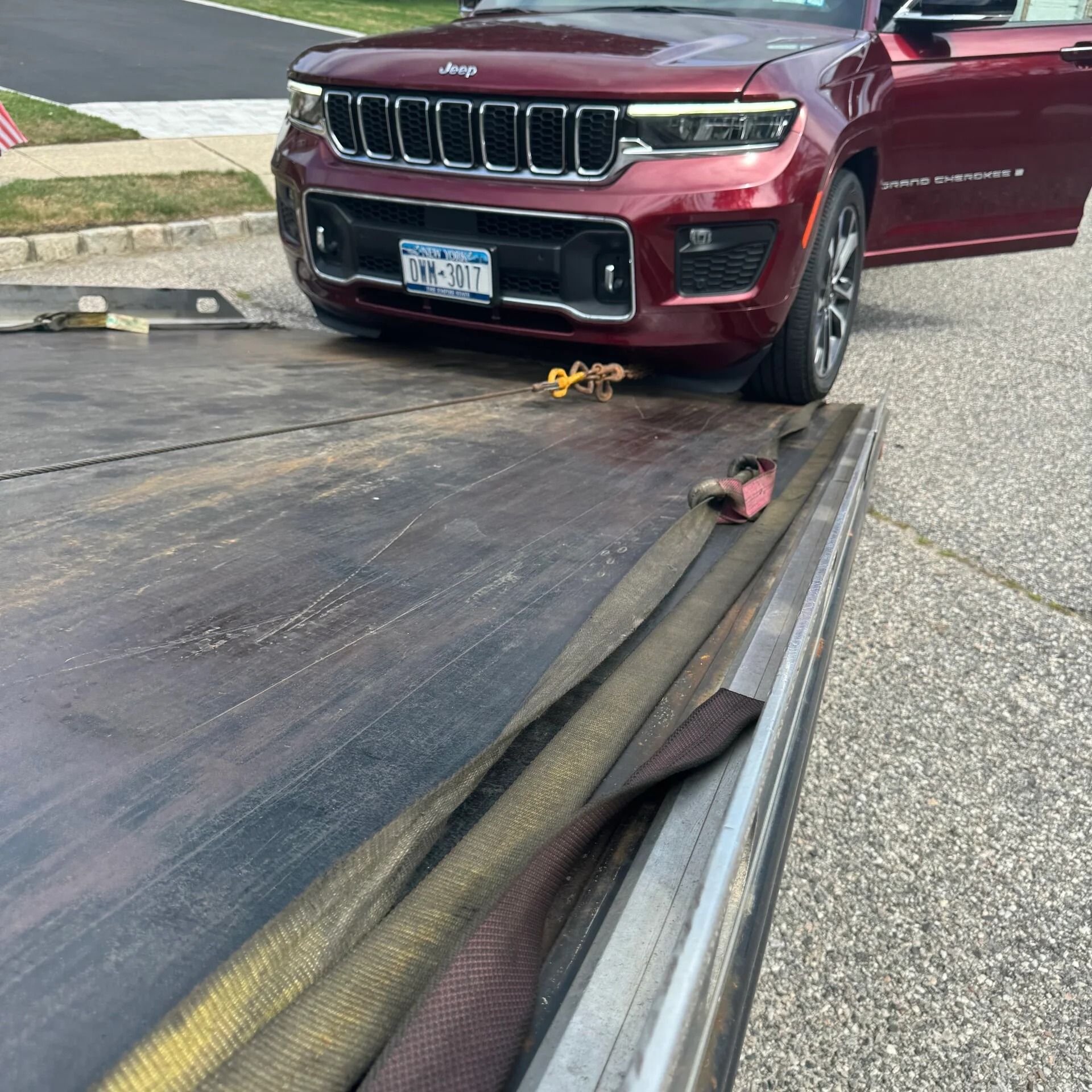 Red Jeep stuck on a rolled-up flatbed trailer ramp on a roadside