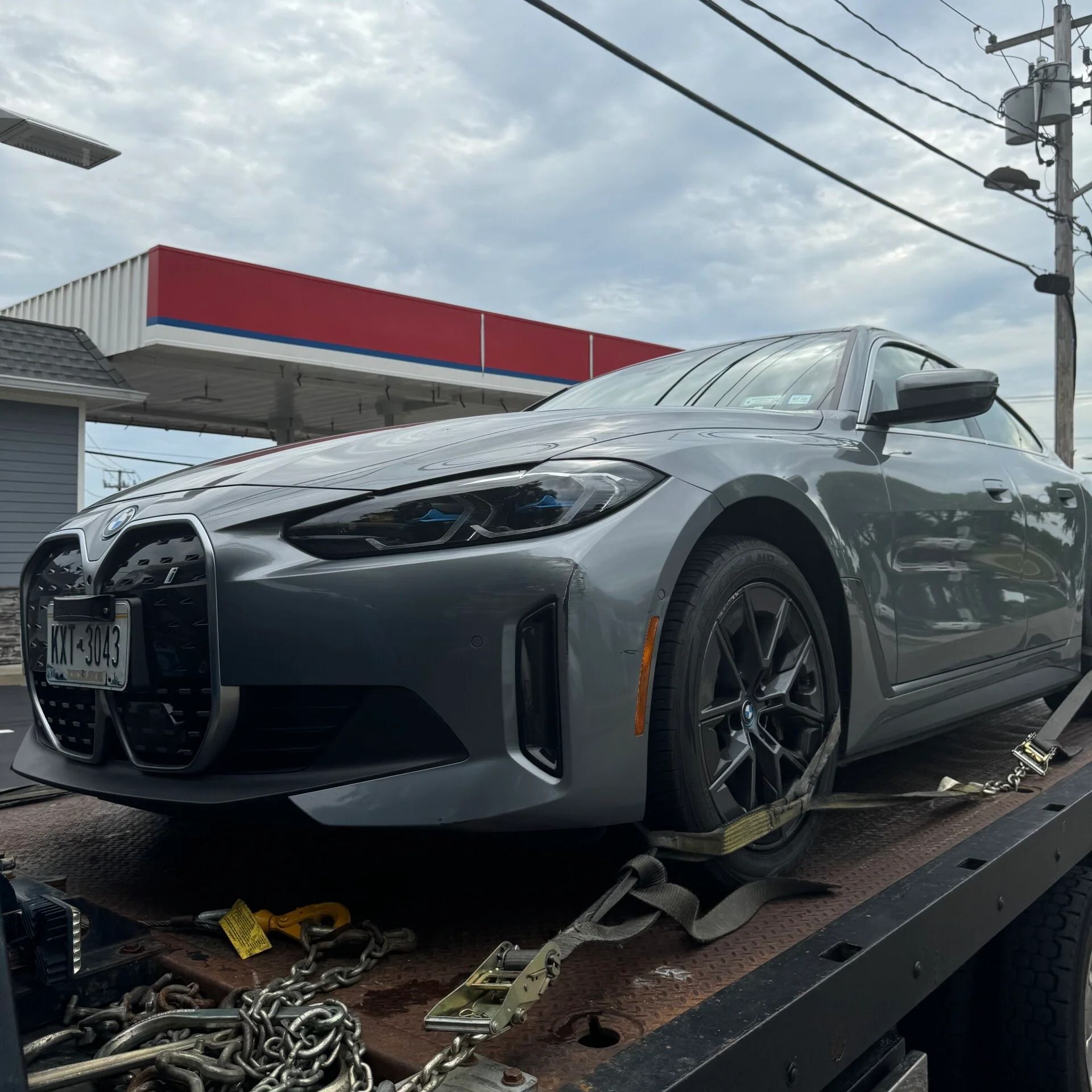 Gray sedan secured on a tow truck, parked outdoors near a gas station