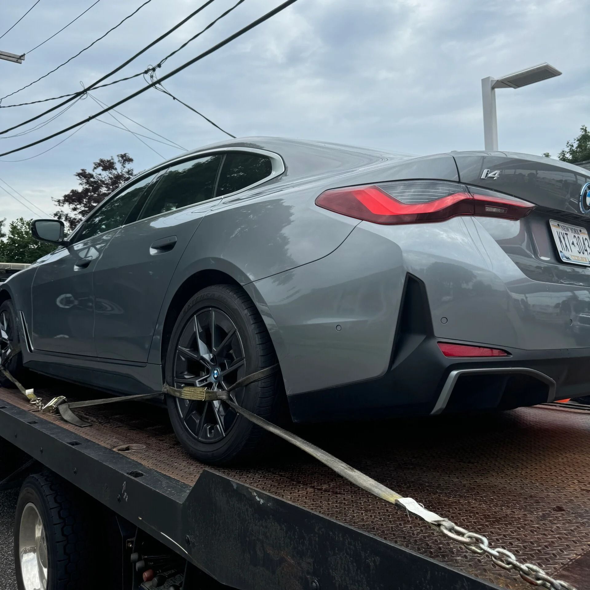 Gray sedan strapped on a tow truck bed under cloudy skies