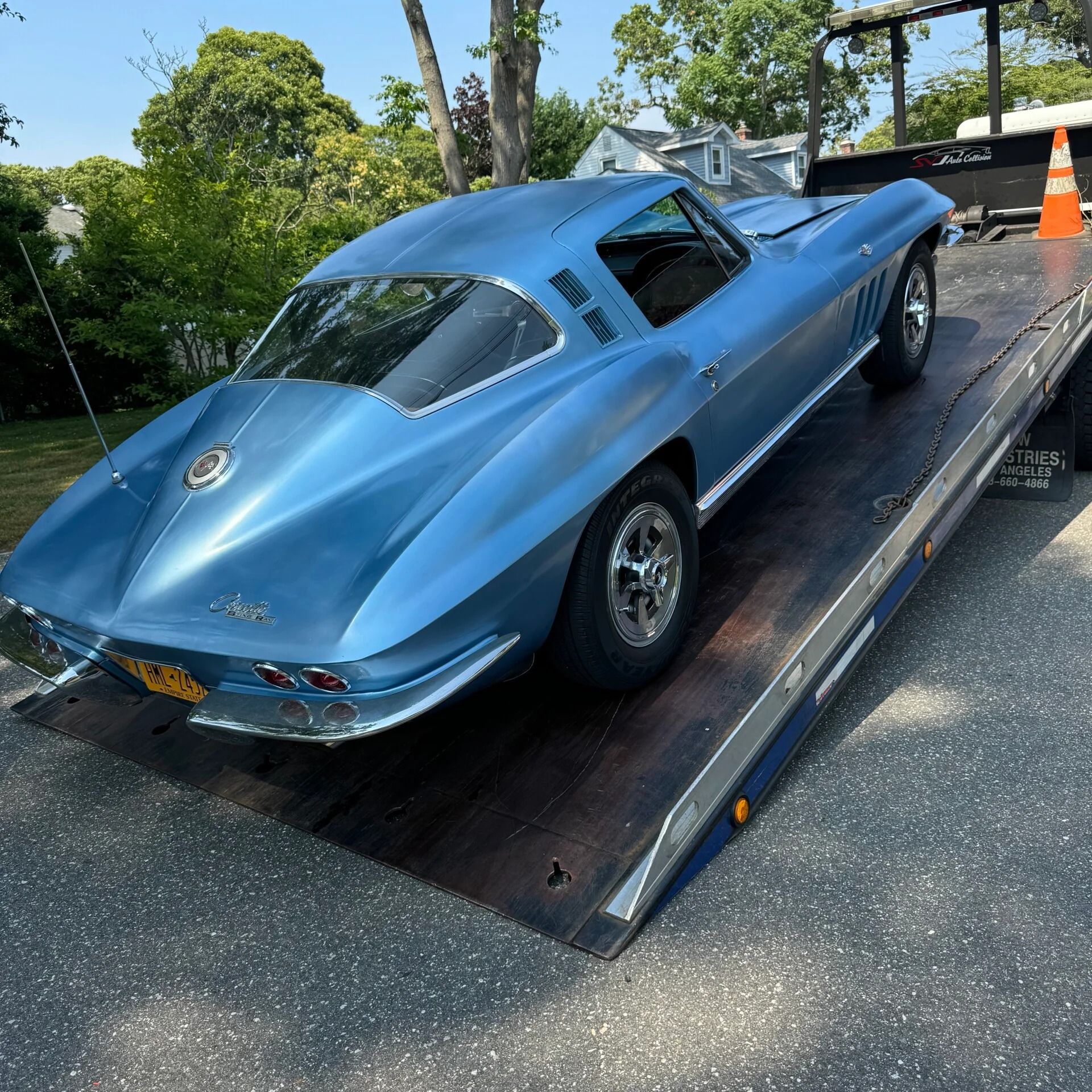 Blue classic sports car on a tow truck ramp in a residential street