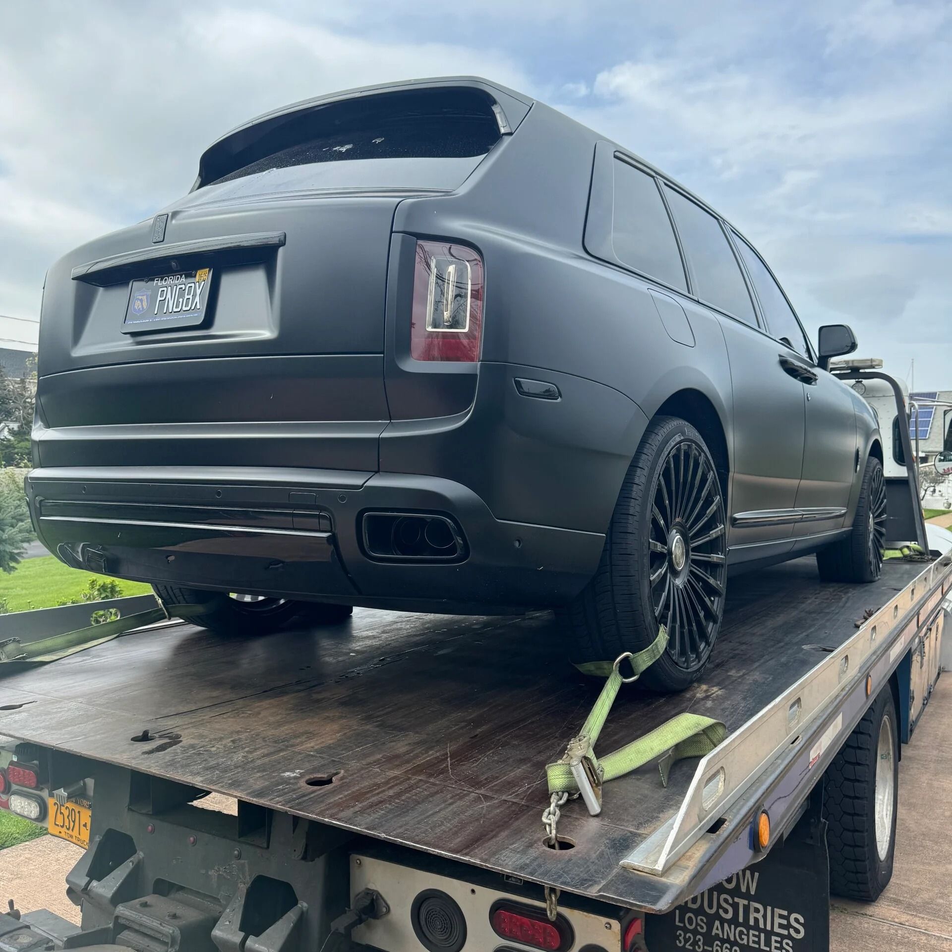 Black Rolls-Royce SUV strapped on a flatbed trailer, viewed from the rear-left.