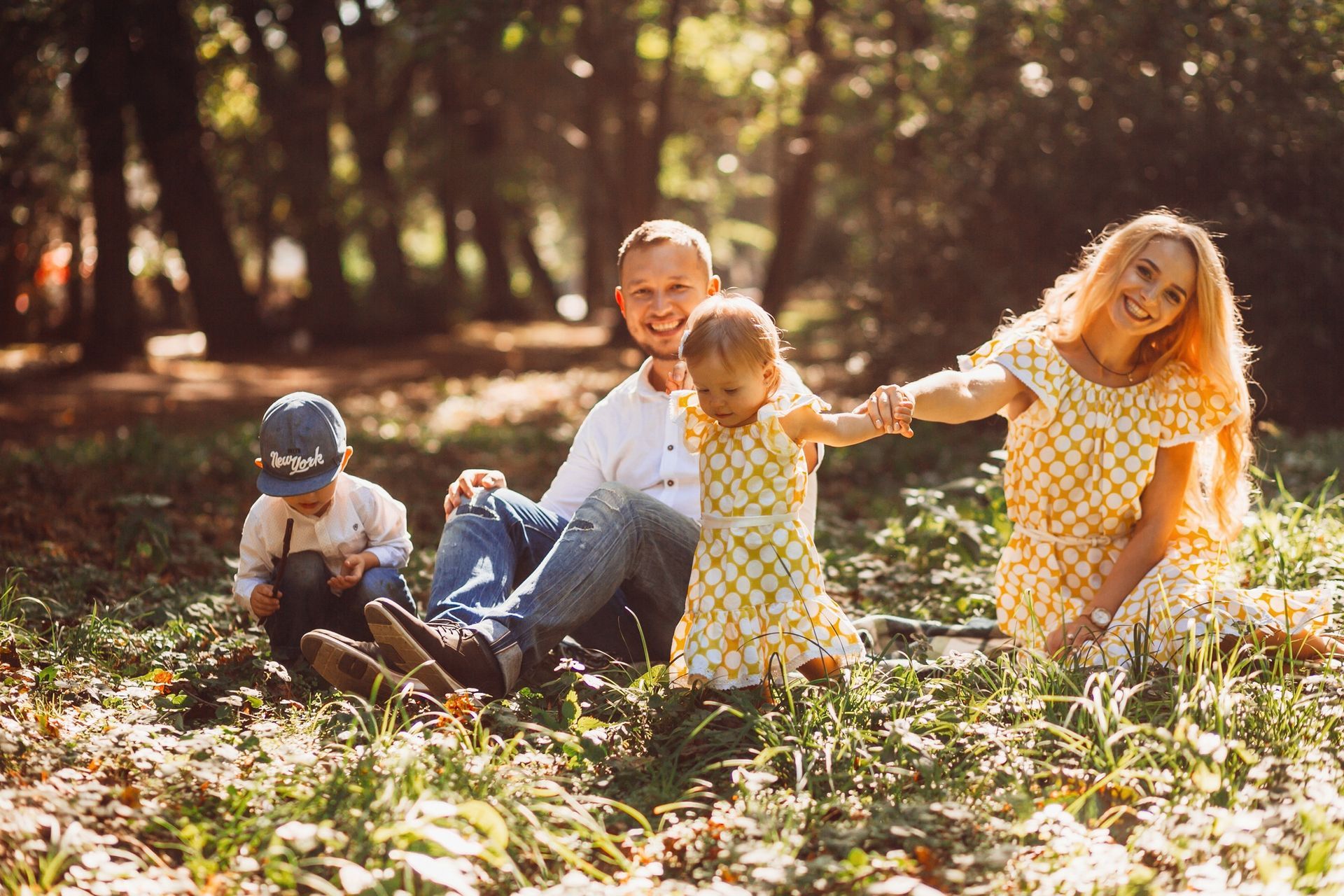 Family sitting in sunlit forest clearing, laughing and playing in the leaves