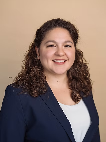 Smiling person in a navy blazer and white top against a beige background