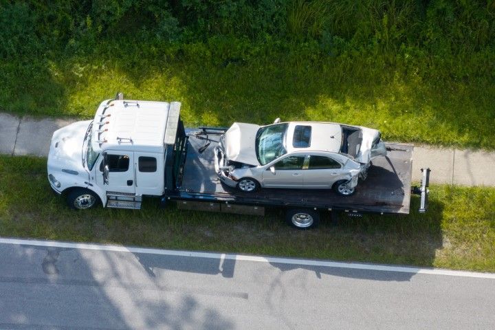 Tow truck hauling a silver car on a flatbed beside a road with grass.