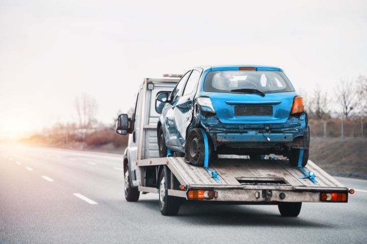 Blue hatchback on a tow truck driving along a road at sunset