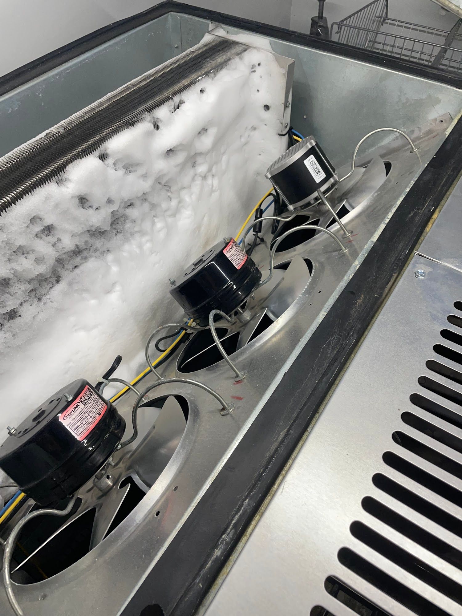 Interior of a freezer with heavy ice buildup on the coils and three small black motors.