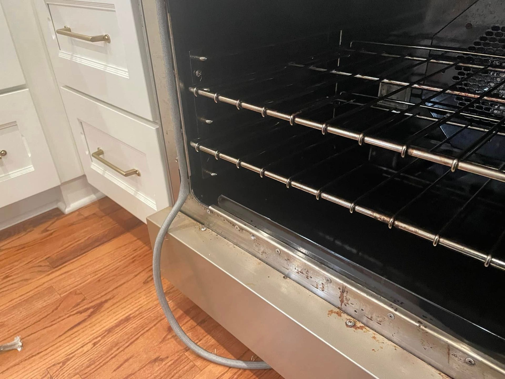 Open oven interior with racks, dirty bottom, next to white cabinets and wood floor.