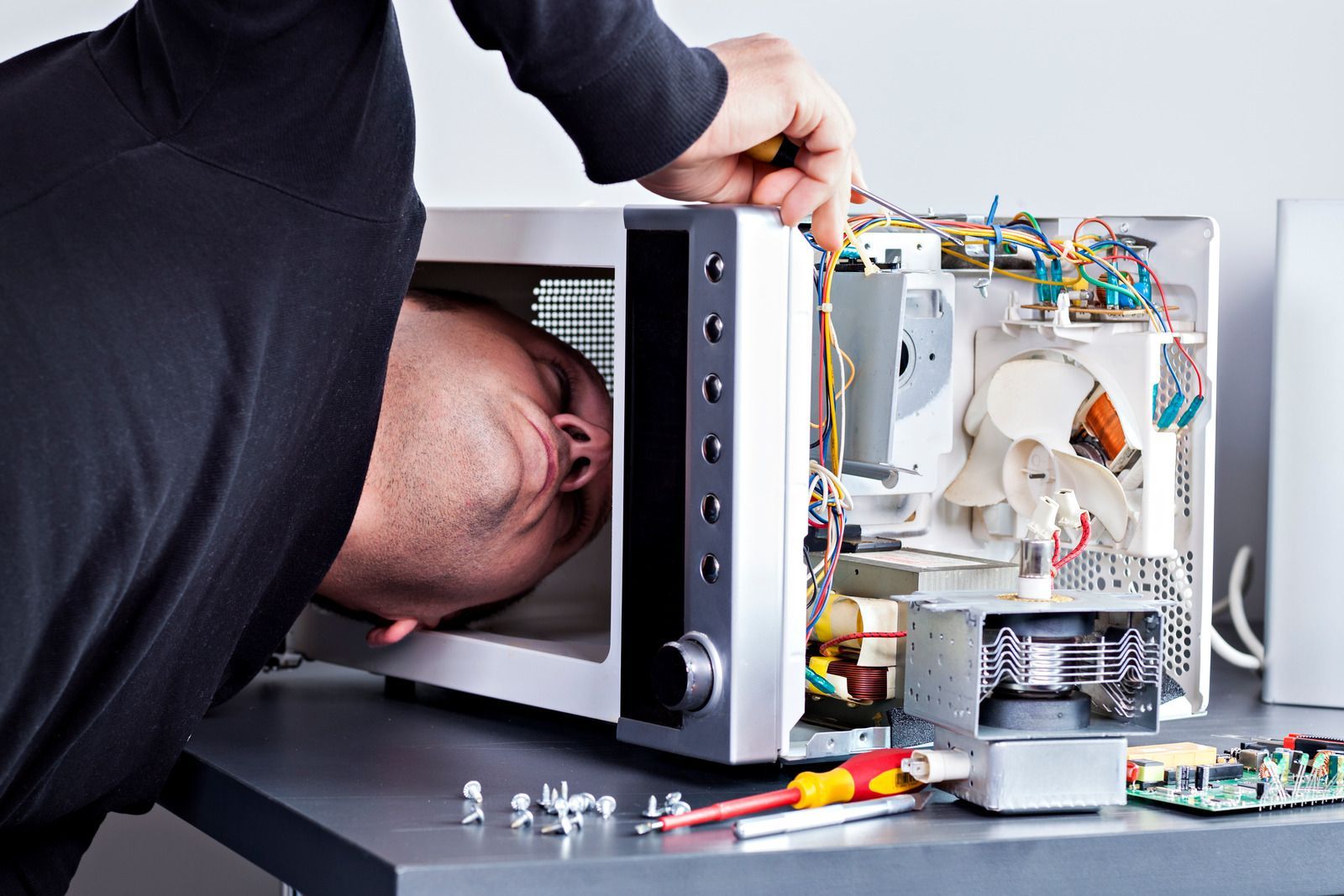 Person repairs a microwave oven, leaning inside with a screwdriver.