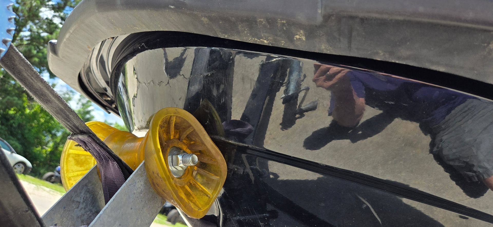 A close-up view of a yellow boat trailer roller pressed against the dark, glossy hull of a boat being trailered.