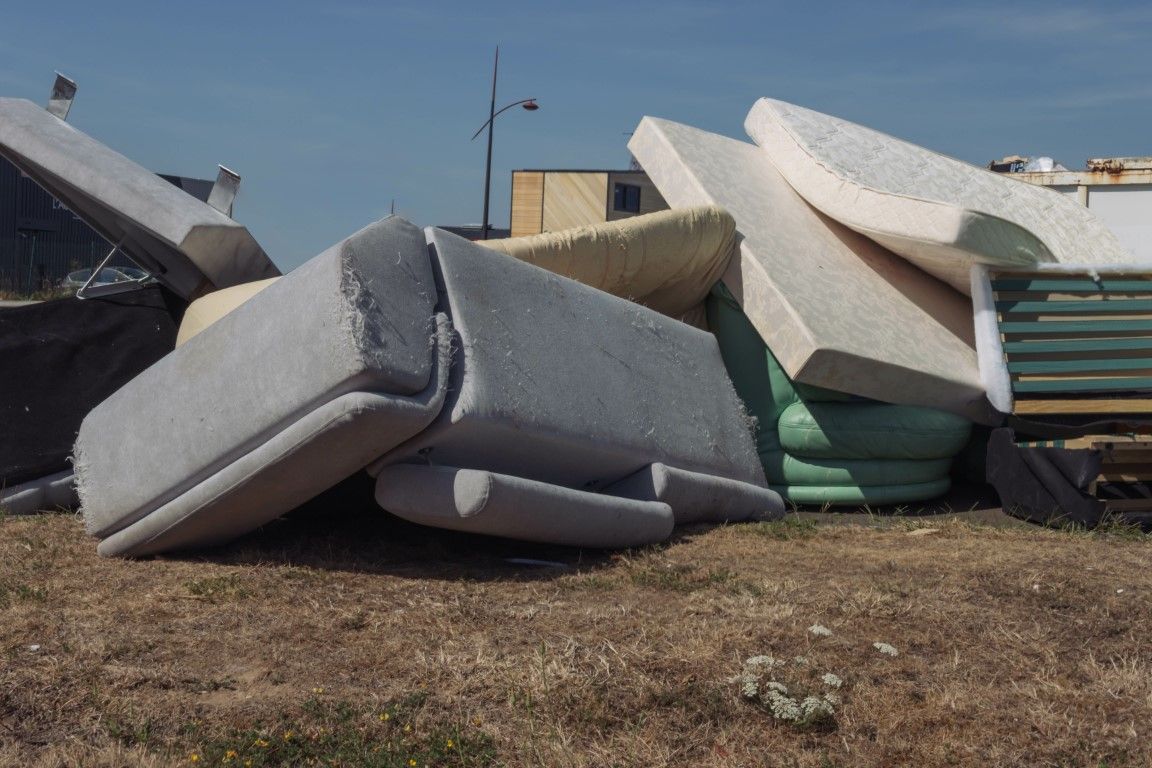 Pile of discarded mattresses and foam cushions outdoors on dry ground