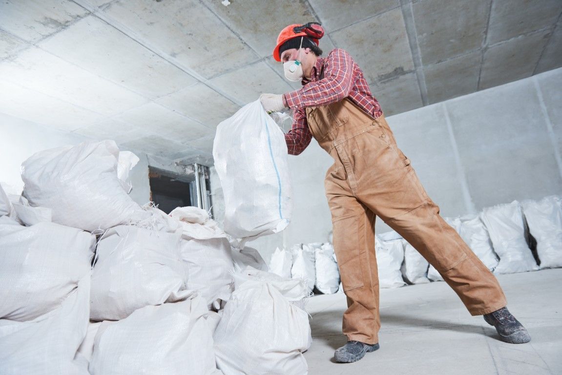 Worker in red helmet and tan overalls loading white sacks in a warehouse
