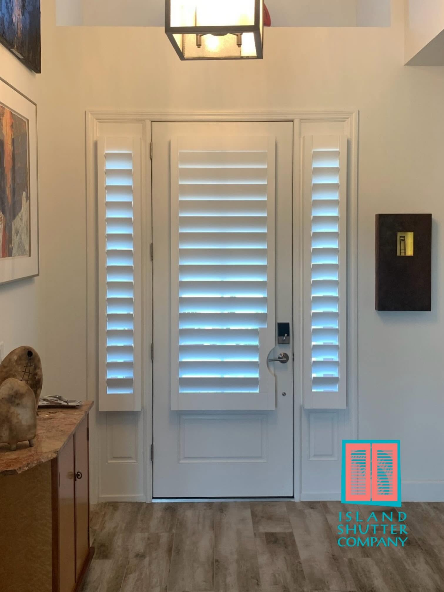 Front entry with white shuttered door, sidelights, wood floor, and wall-mounted mailbox.