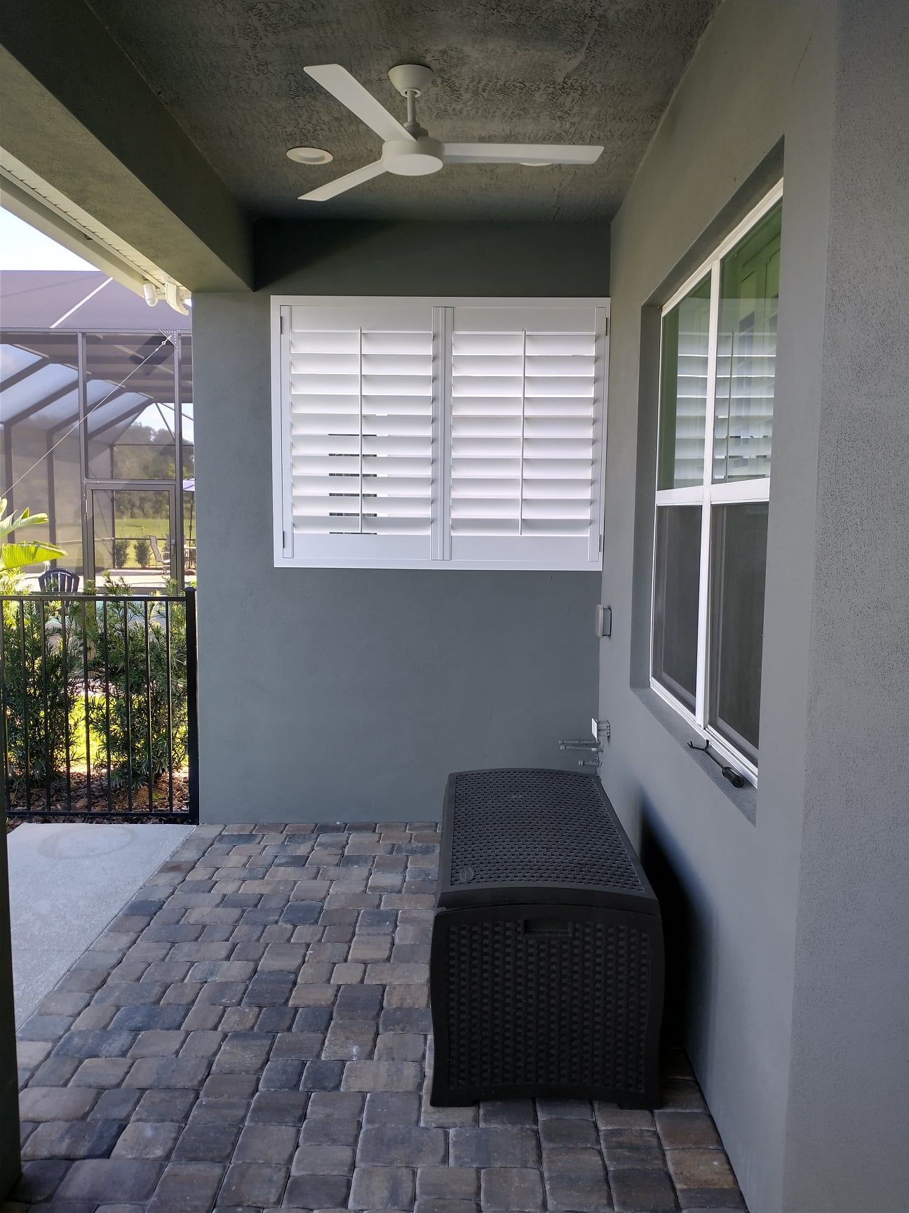 Covered patio with paver floor, shuttered window, ceiling fan, and outdoor storage bench seating are.