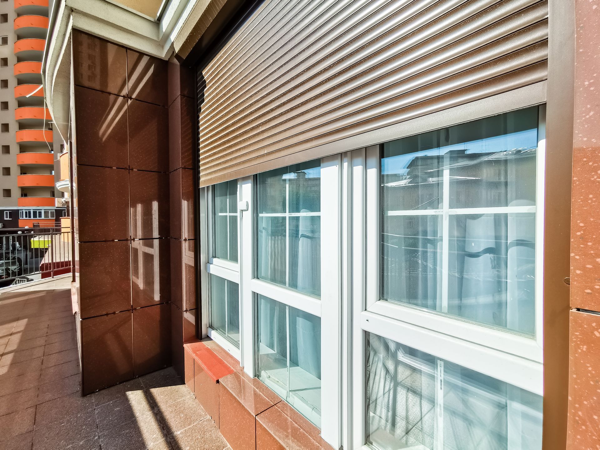 Exterior windows fitted with metal roller shutters on a modern residential building balcony.