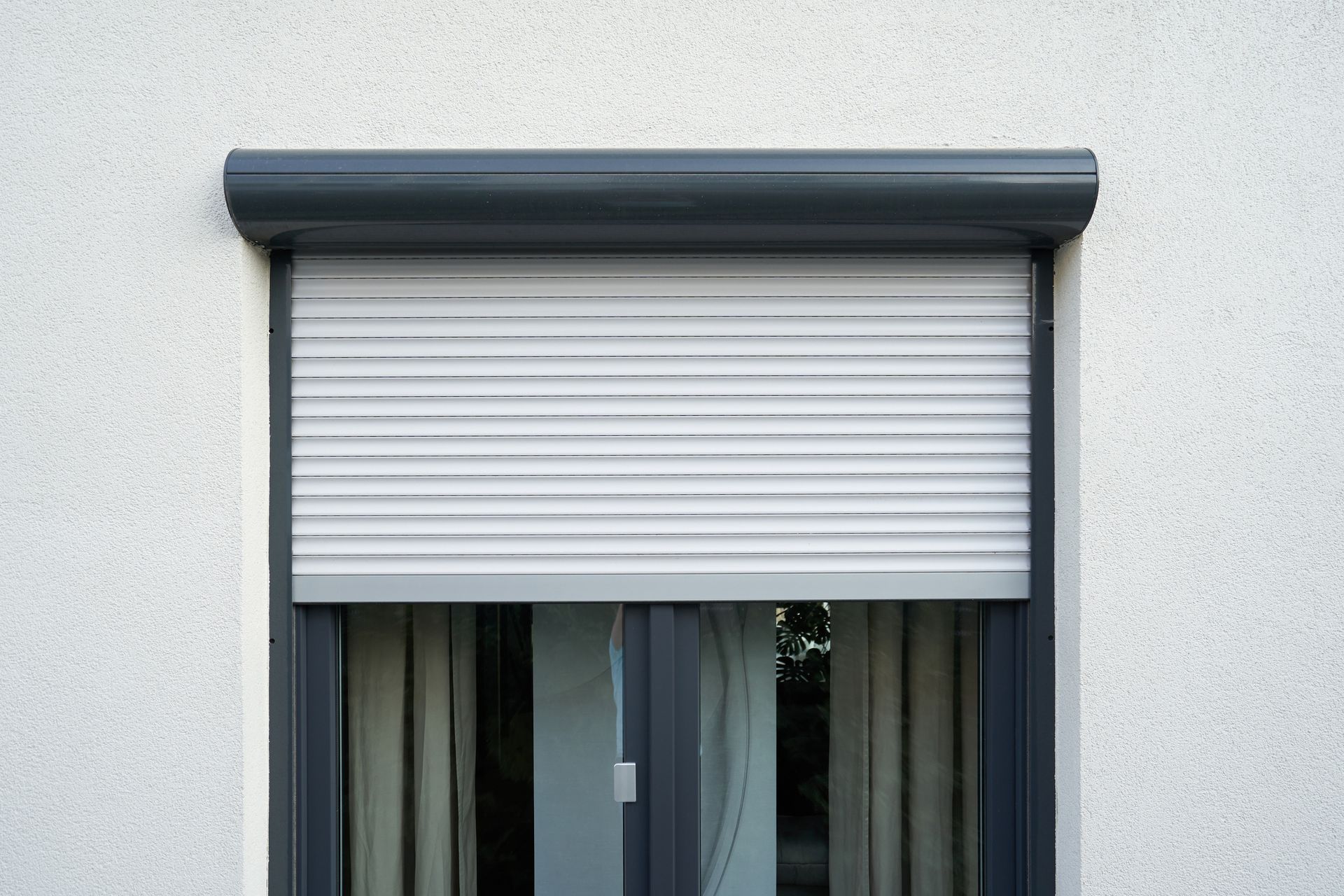 White exterior roller shutter on gray aluminum window frame on stucco wall.