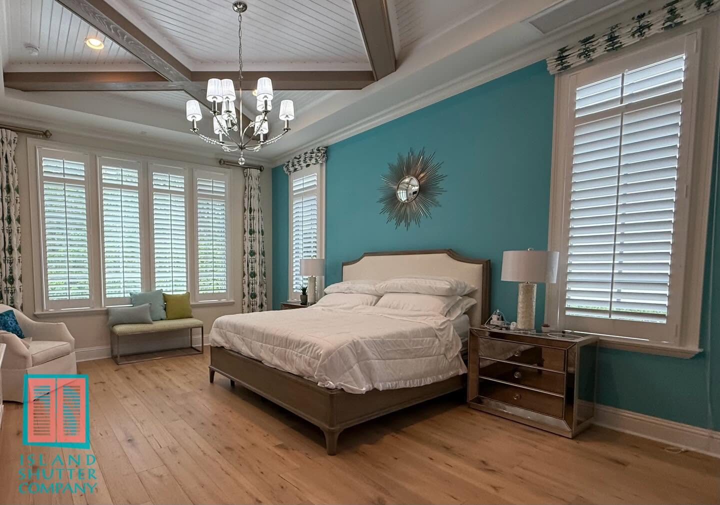 Bright bedroom with turquoise accent wall, white bed, chandelier, and wood floors.