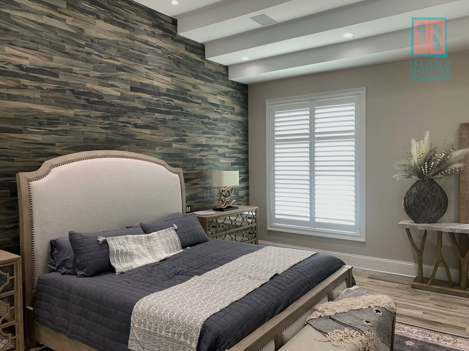 Elegant bedroom with a beige upholstered bed, dark accent wall, and window with white shutters