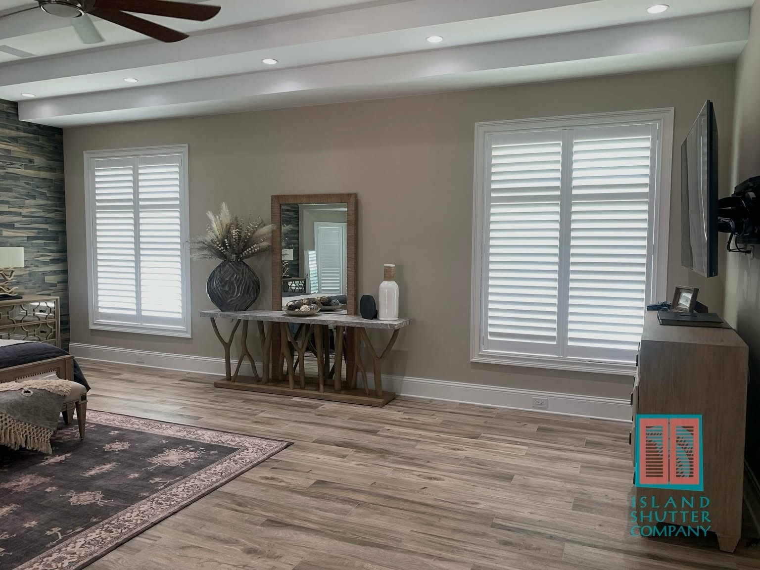 Bright living room with large windows, wood floors, console table, mirror, and wall-mounted TV
