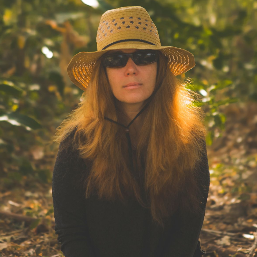 Woman wearing sunglasses and a straw hat in a forest.