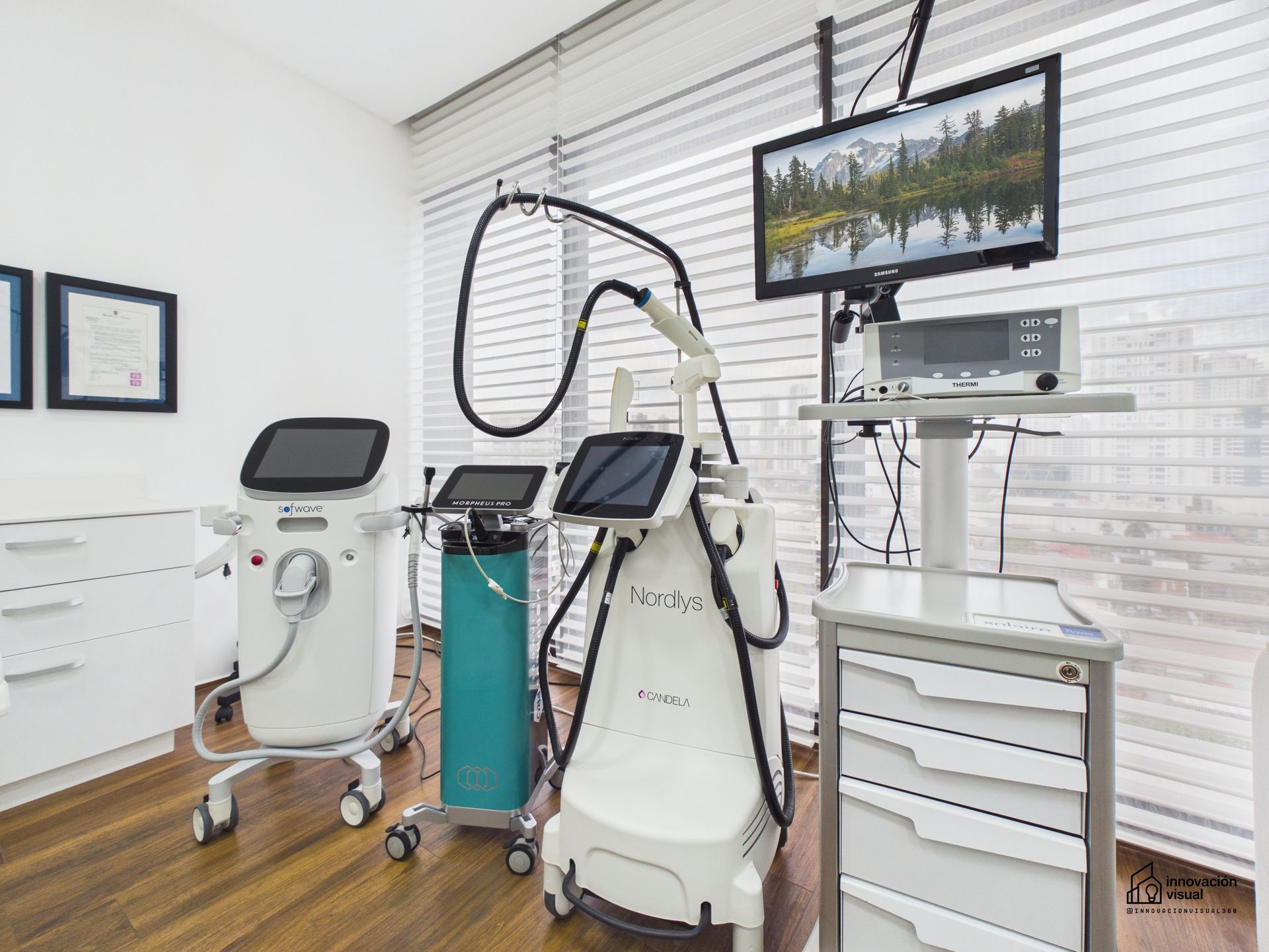 Sala de exploración médica equipada con varios aparatos especializados de terapia láser, equipos de diagnóstico y un monitor.