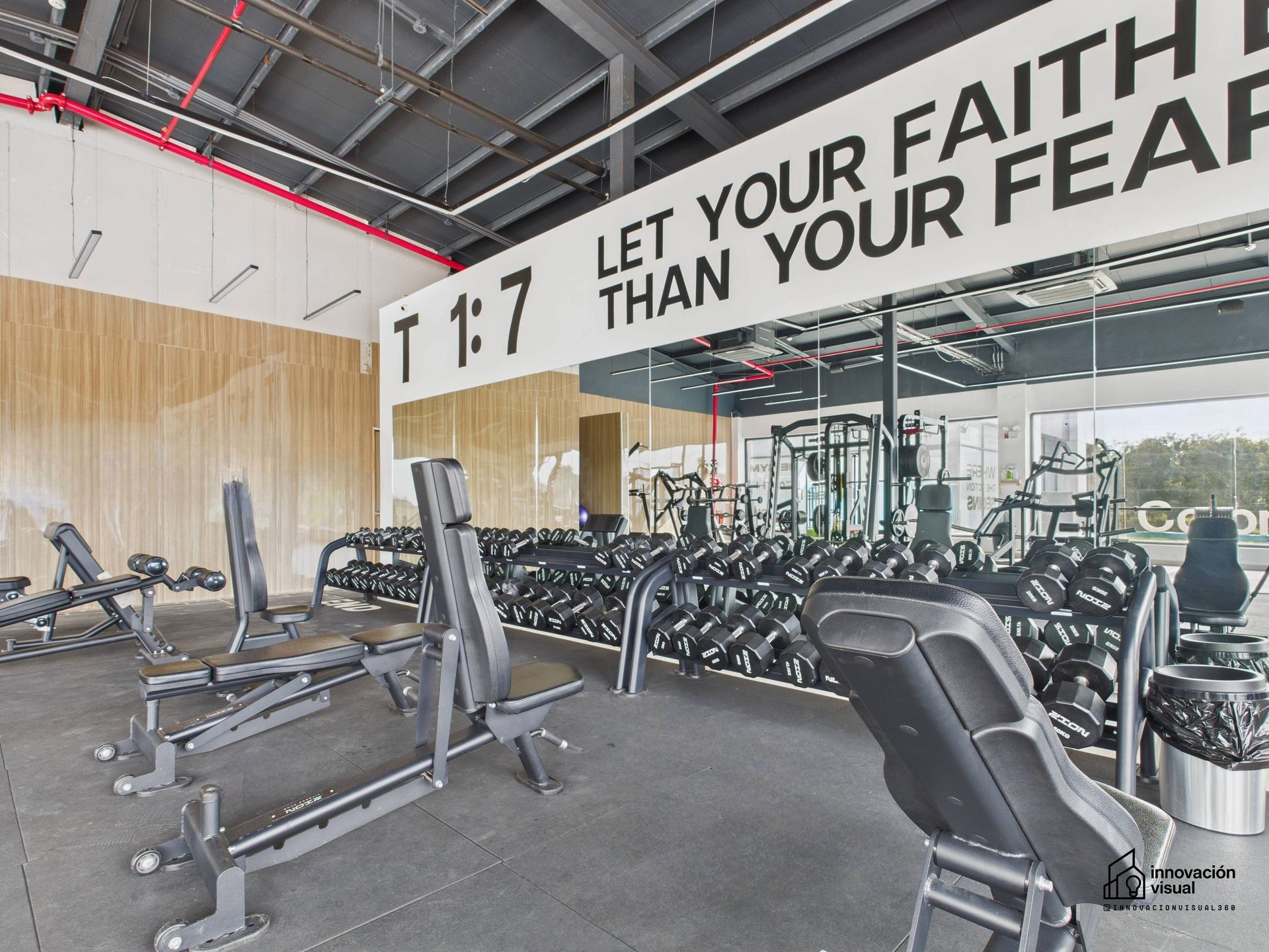 Interior de gimnasio con pesas, bancos y cita motivacional
