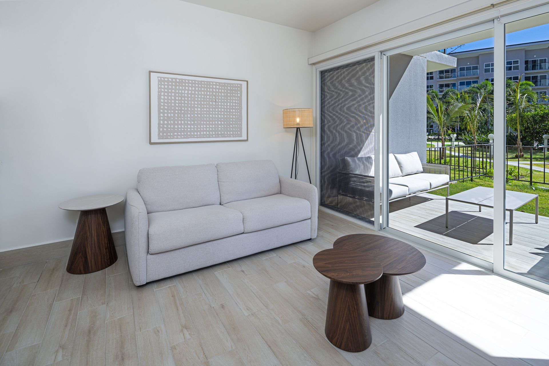Una sala de estar moderna con un sofá, dos mesas y una puerta corrediza que conduce a un patio.