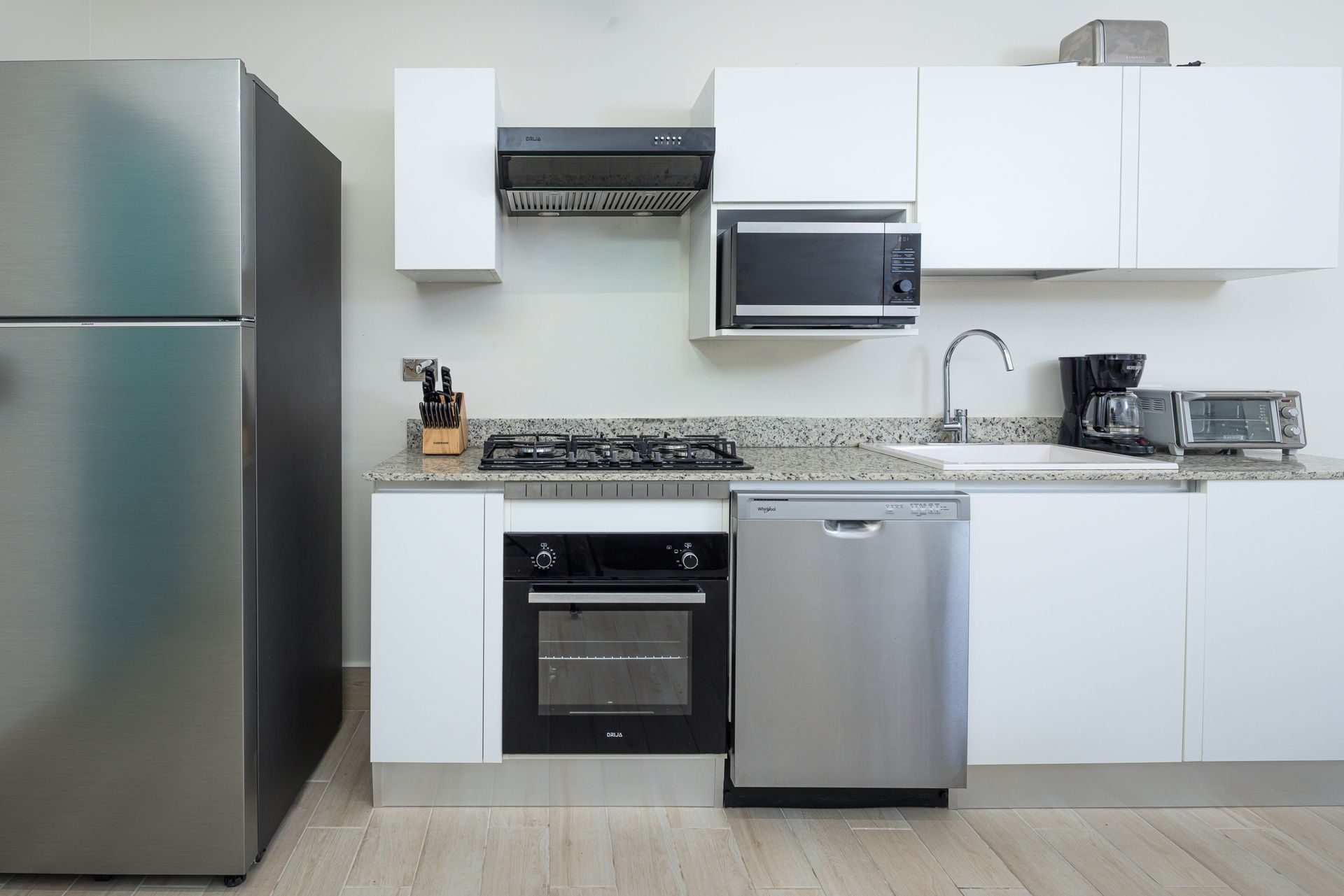 Cocina moderna blanca con electrodomésticos de acero inoxidable: frigorífico, horno, lavavajillas, microondas.