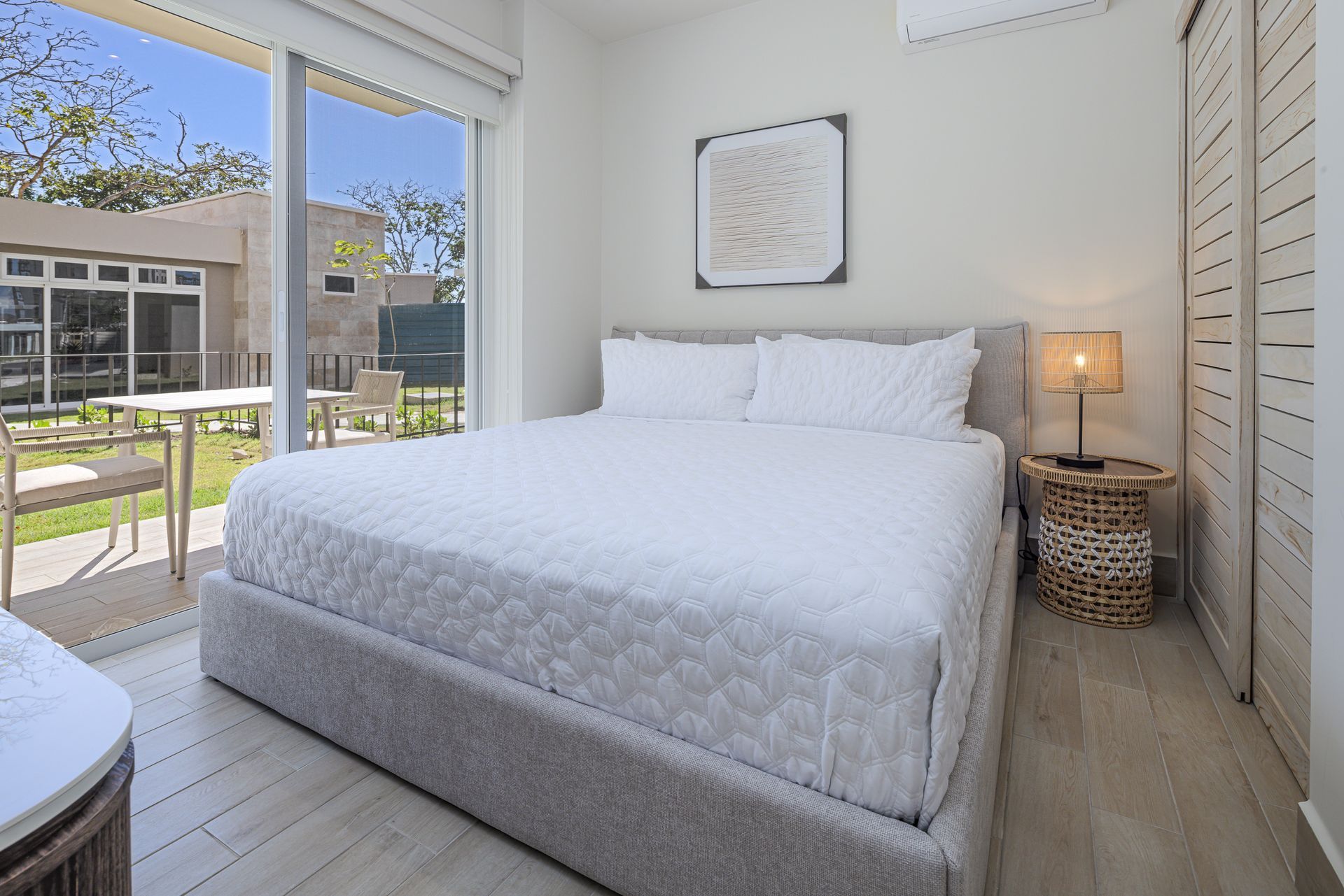 Dormitorio con cama queen, pisos de madera clara y acceso al patio.