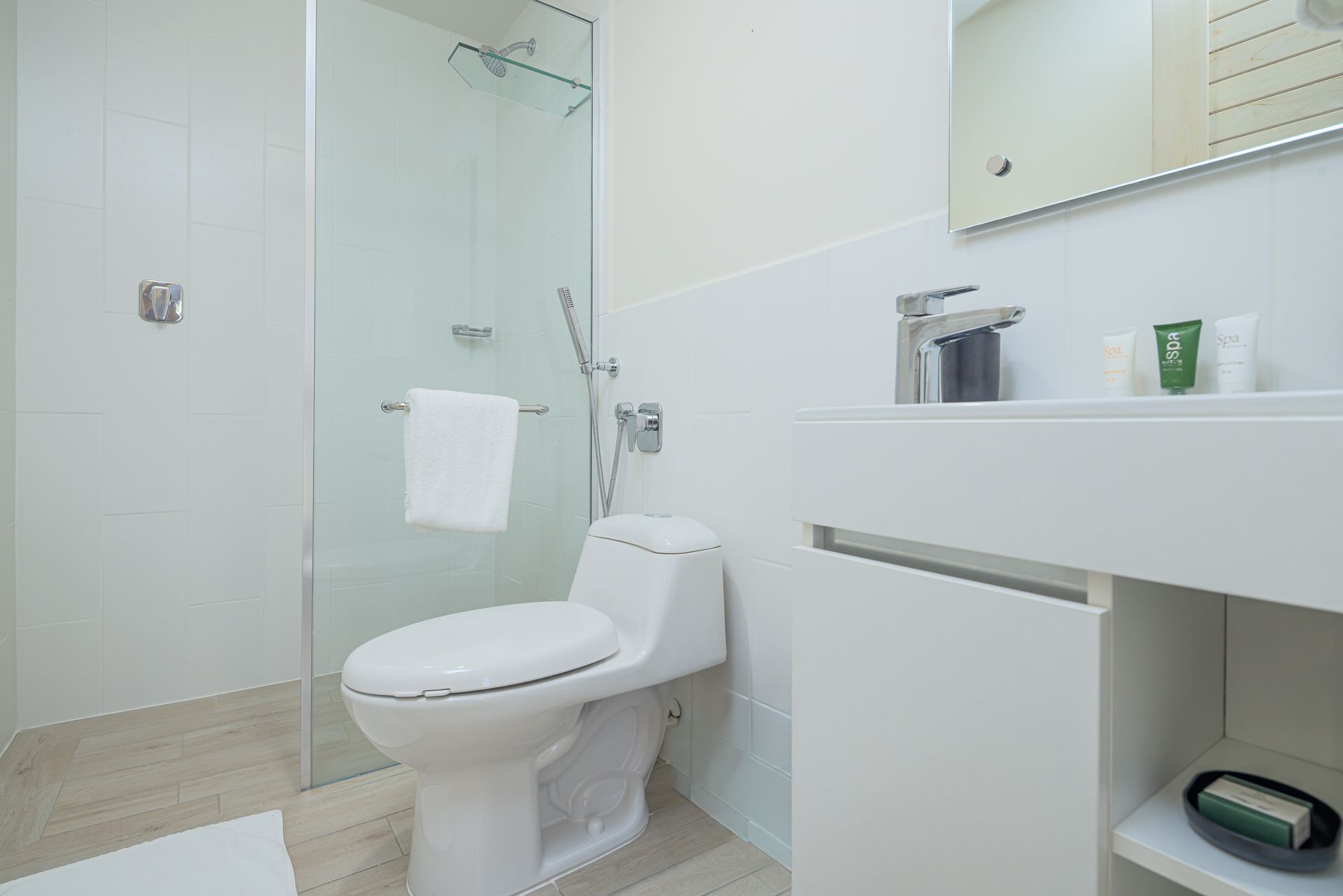 Baño blanco brillante con ducha de cristal, inodoro y lavabo.