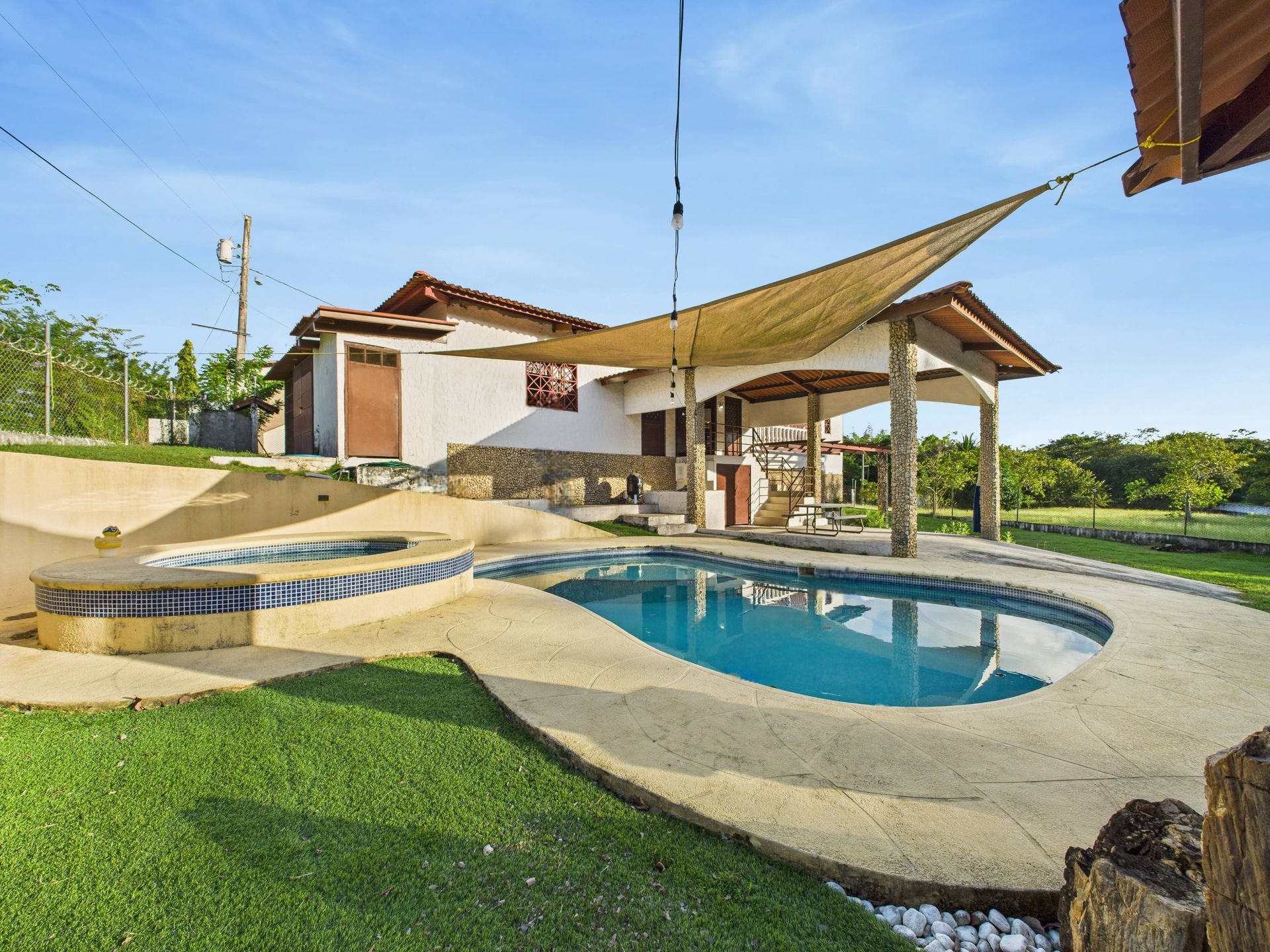 Área de piscina y patio con casa, agua azul y césped verde.