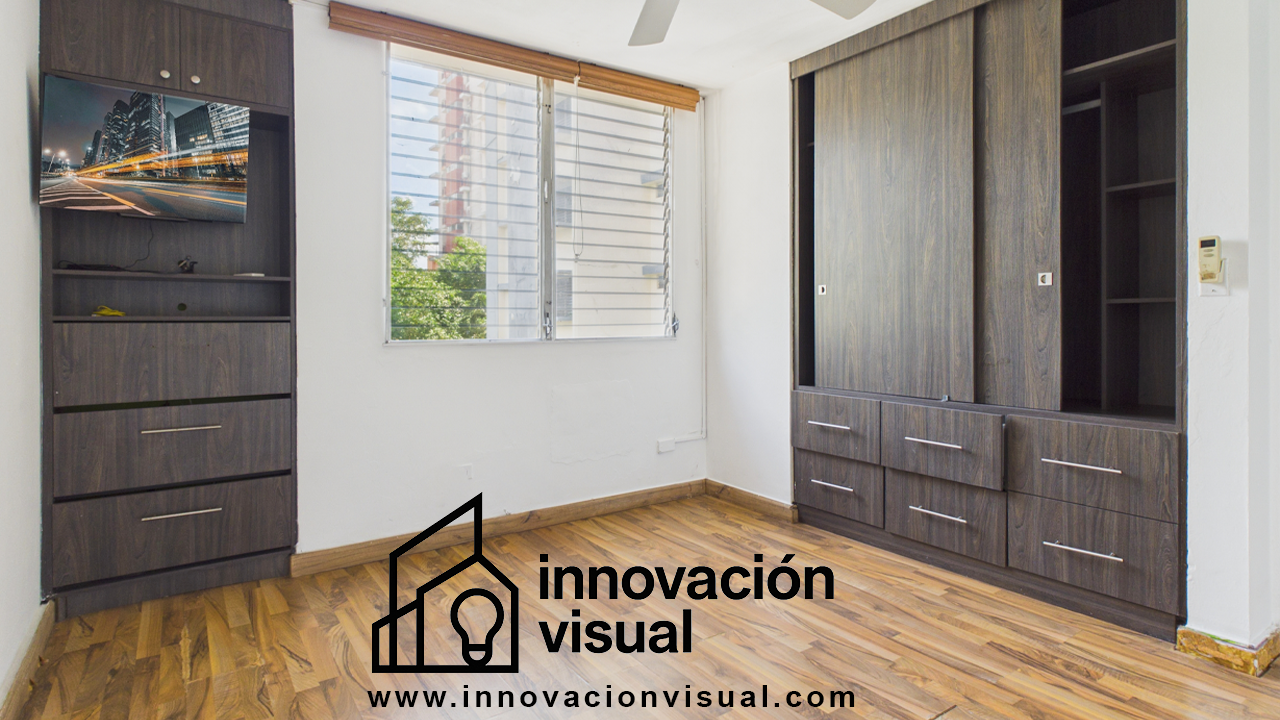 Dormitorio con gabinetes y cajones de madera oscura, piso de madera, ventana y TV montada en un gabinete alto.