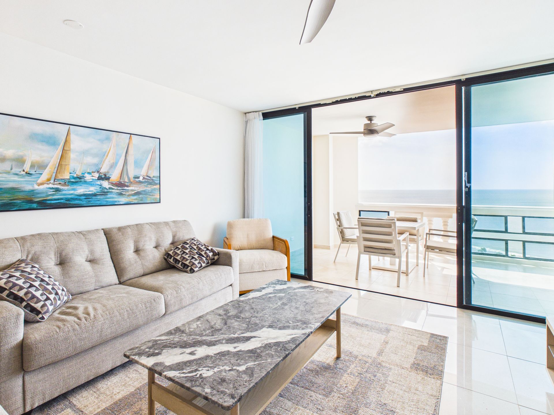 Luminoso salón con sofá beige, mesa de centro, cuadro con motivos marinos y puertas correderas que dan a un balcón con vistas al mar.coronado country club