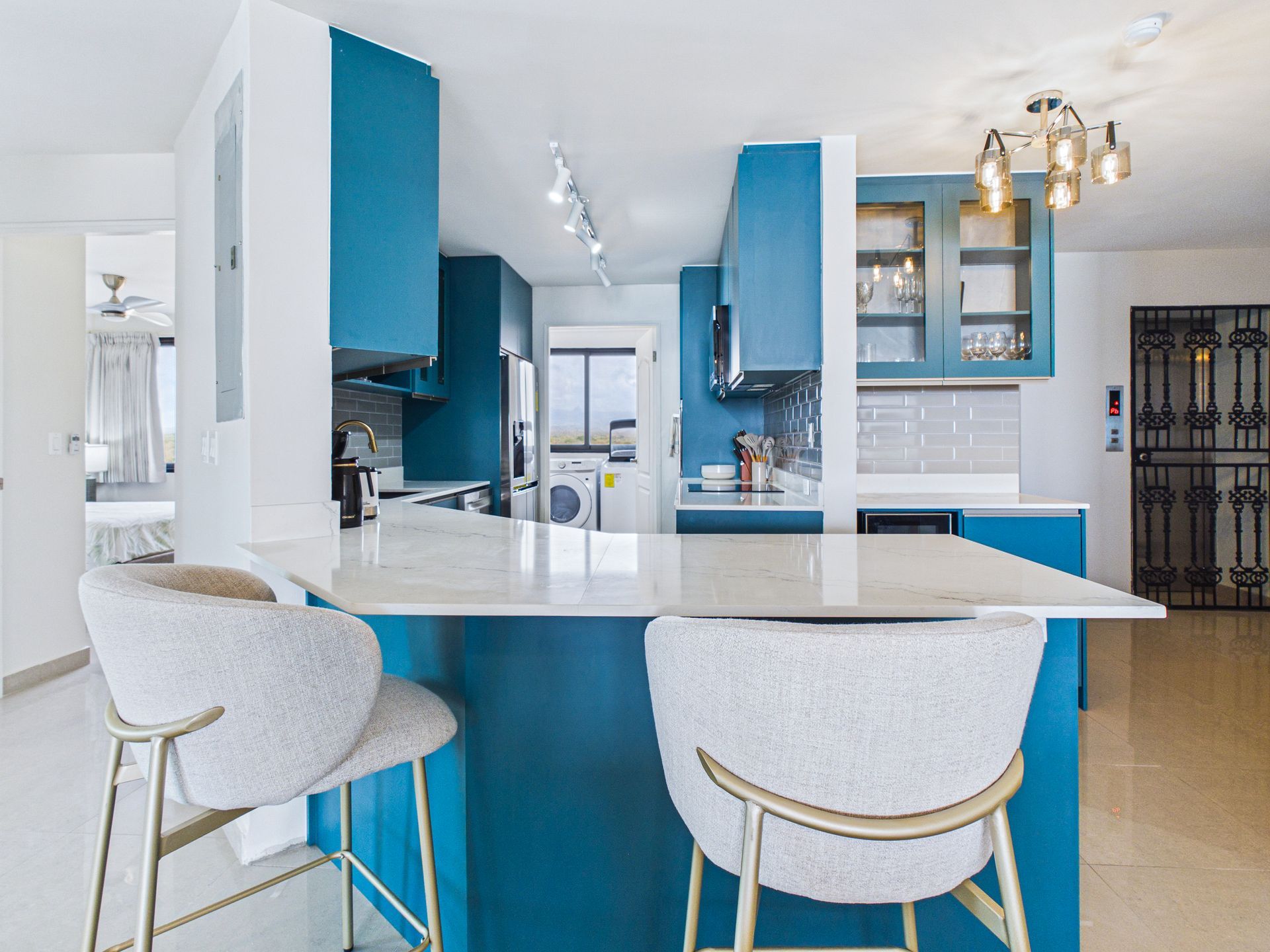 Cocina moderna con gabinetes azules, isla blanca y lámparas colgantes doradas, vista desde un espacio abierto y luminoso.coronado country club