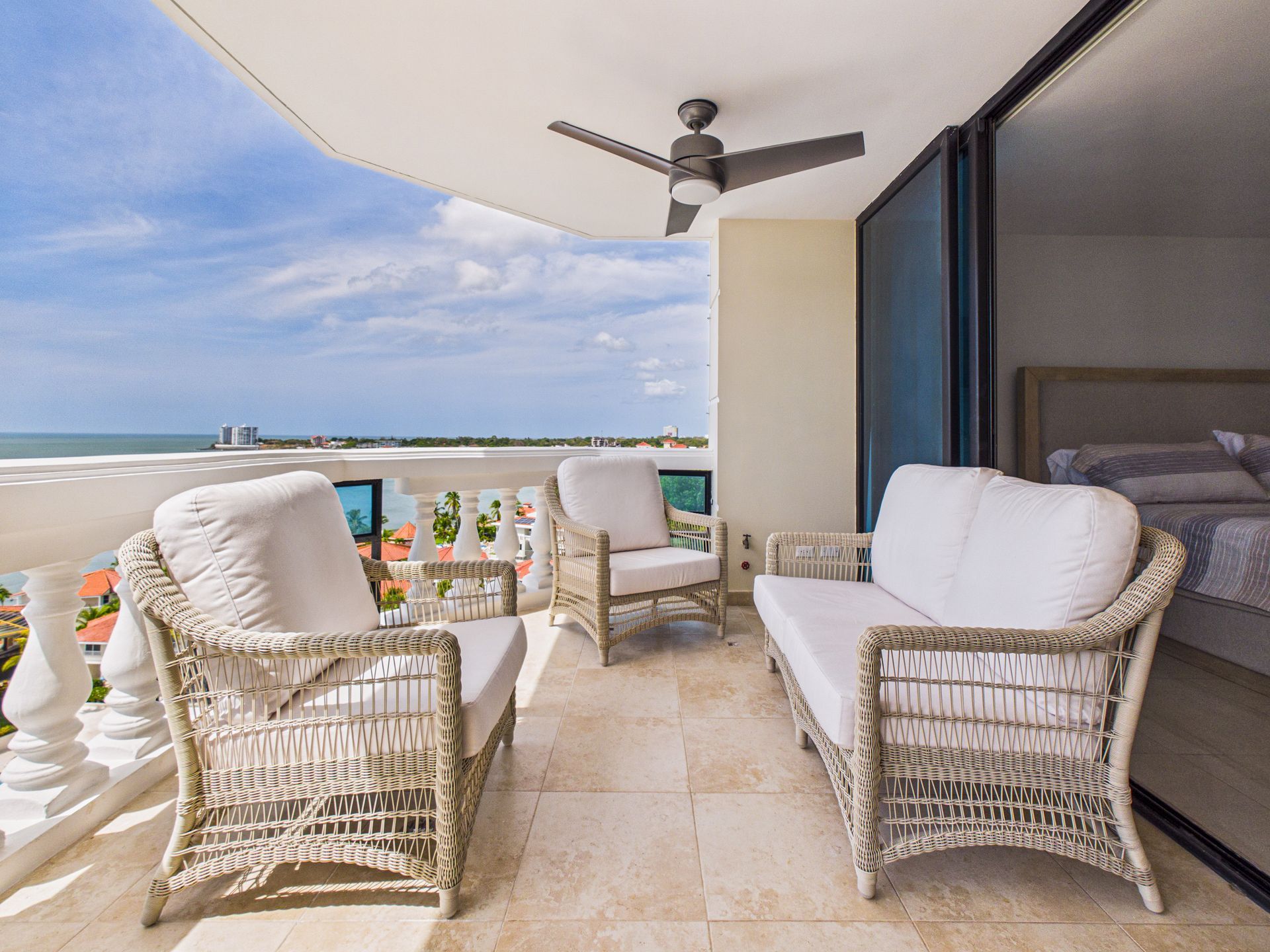 Balcón con asientos de mimbre con vistas al océano, bajo un ventilador de techo blanco y un cielo azul despejado.coronado country club