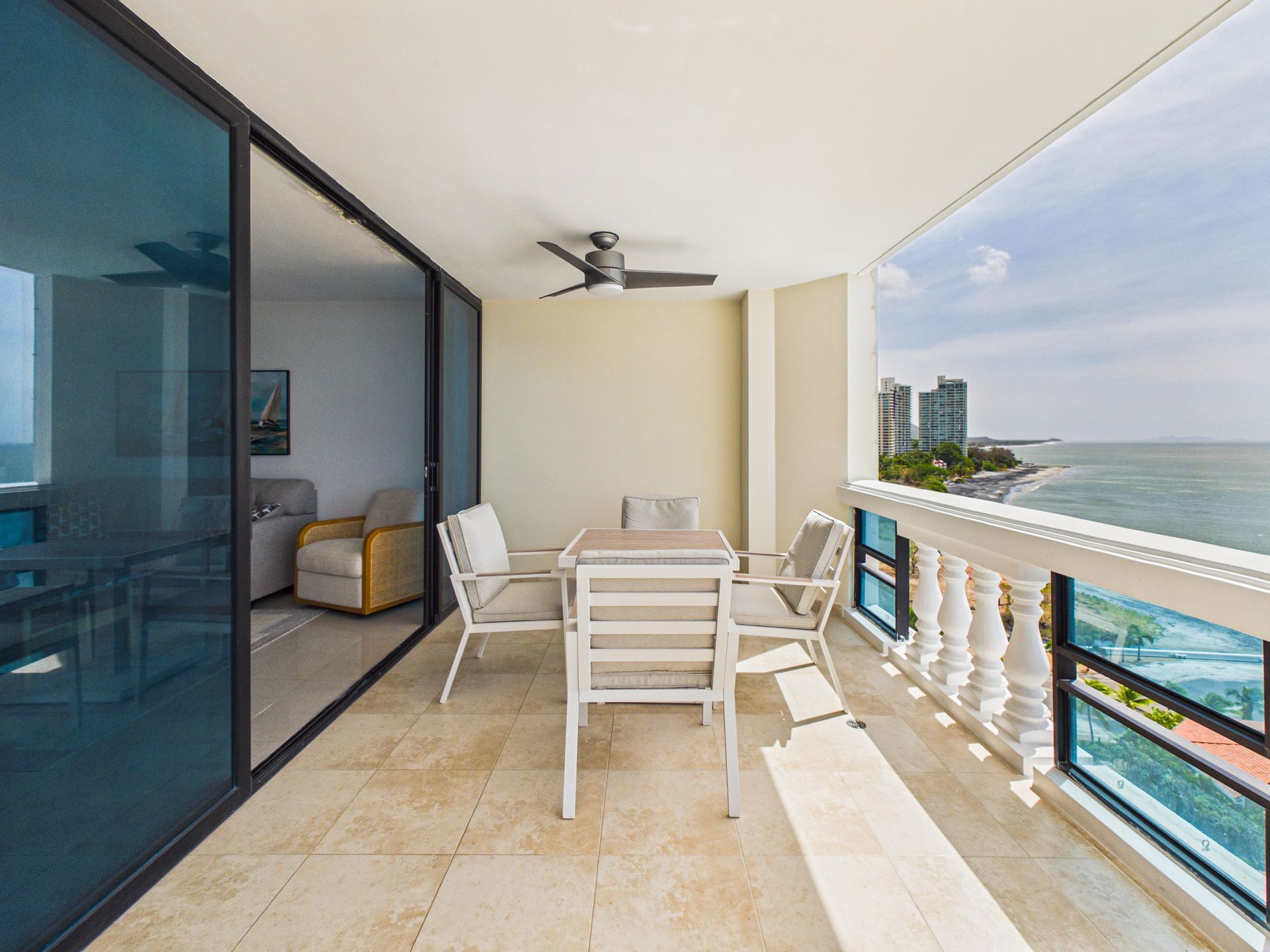 Balcón con sillas y mesa blancas con vistas al océano, con puertas de cristal y ventilador de techo.coronado country club