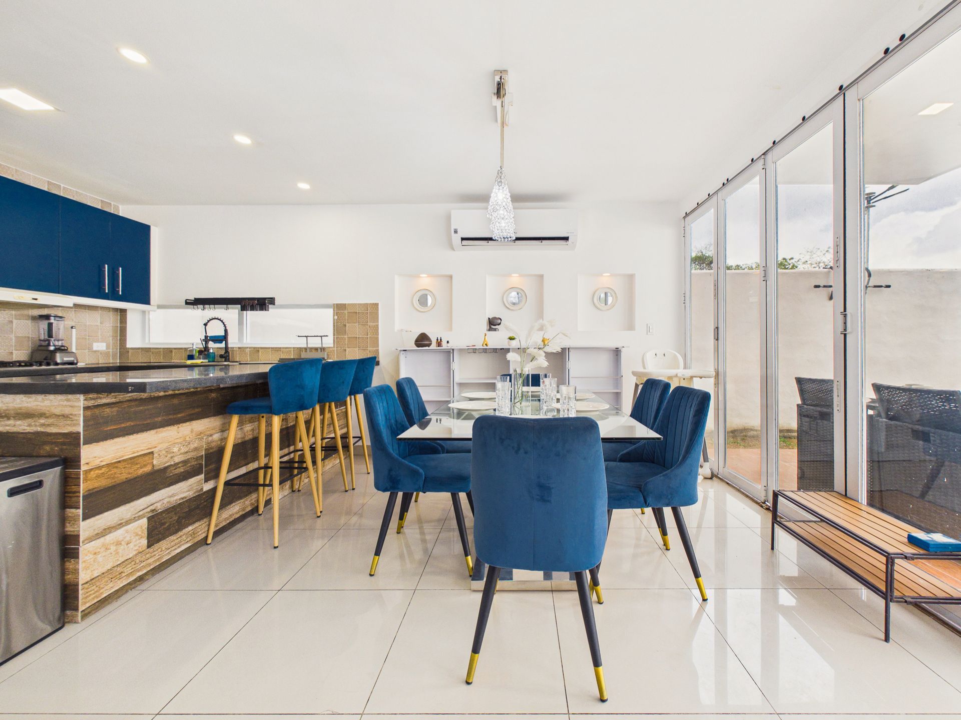 Comedor moderno con sillas azules, mesa blanca y cocina abierta con taburetes de bar.