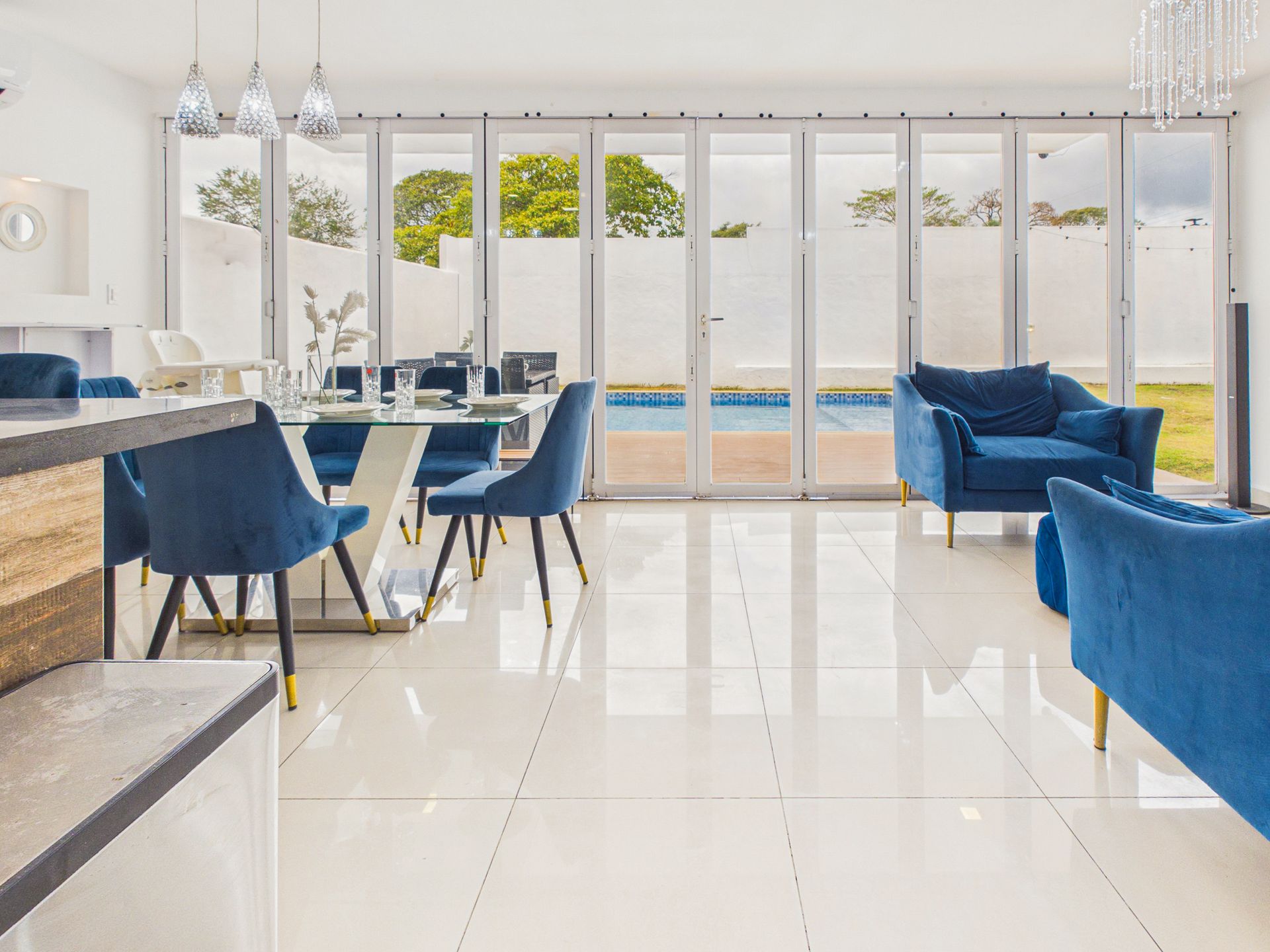 Luminoso salón-comedor moderno con sillas y sofás azules y vistas al océano a través de grandes ventanales.