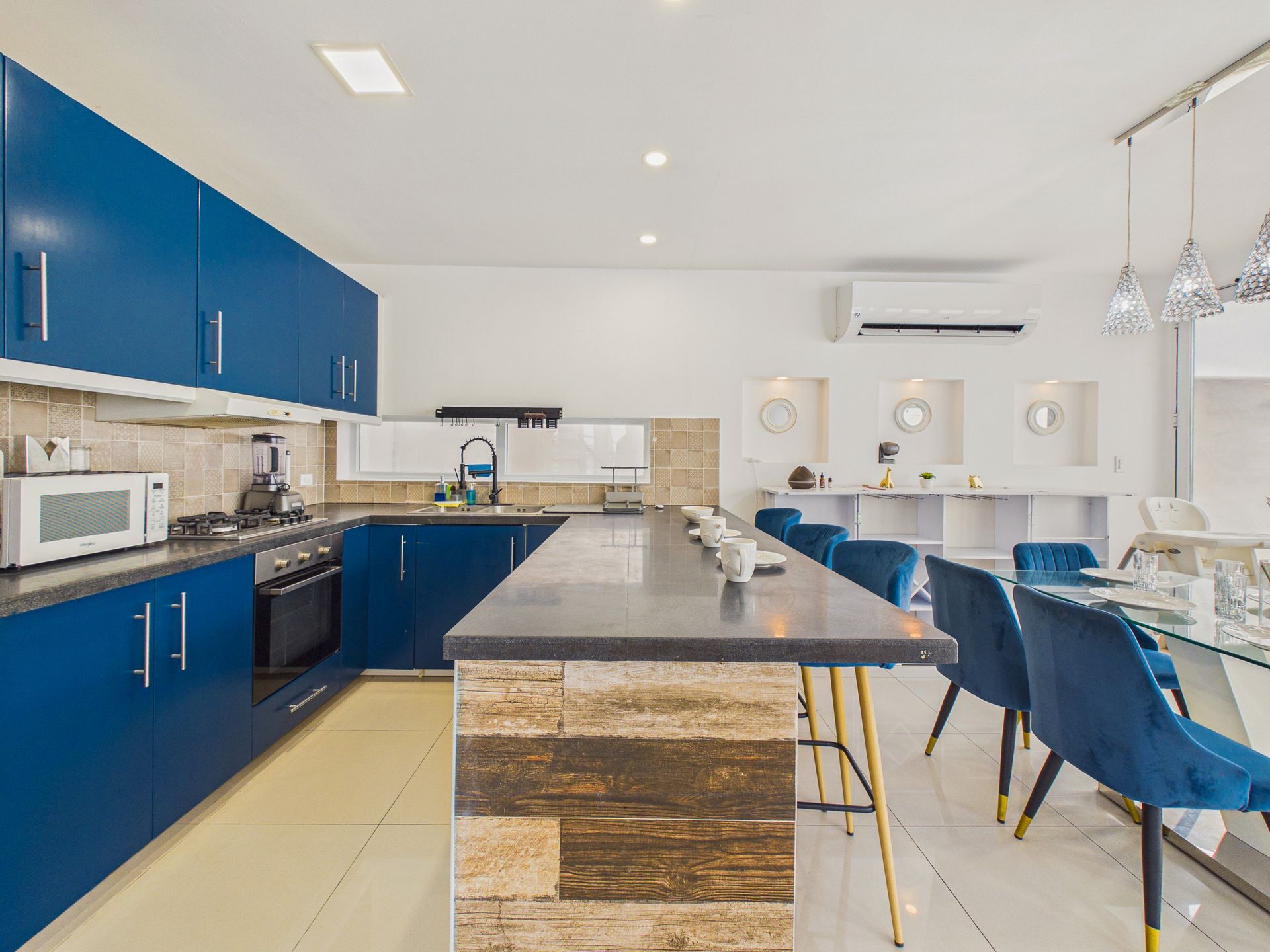 Cocina moderna con gabinetes azules, isla central, sillas de comedor y paredes y luces de techo blancas.
