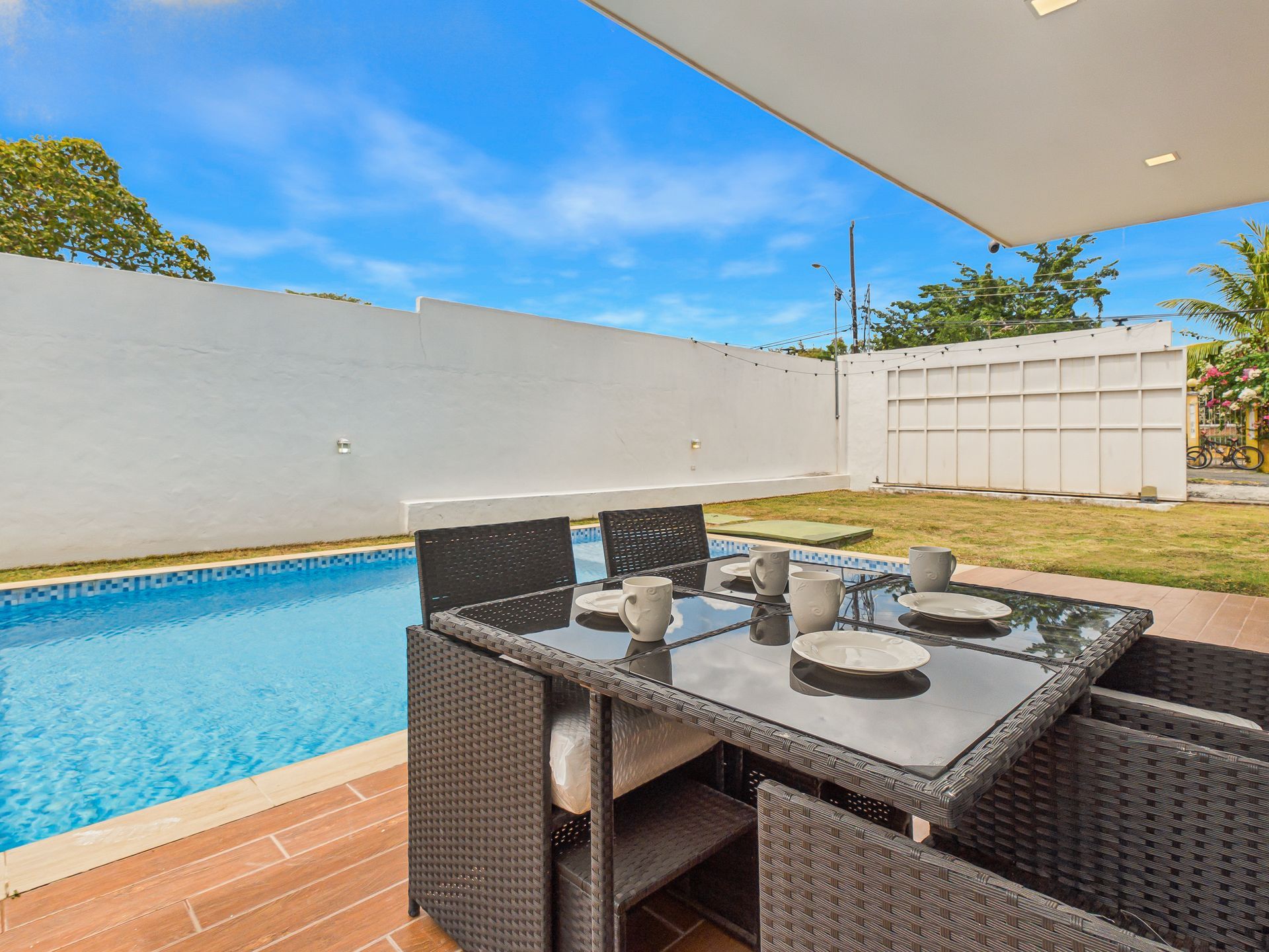 Mesa de comedor en el patio junto a una piscina azul en un jardín moderno.