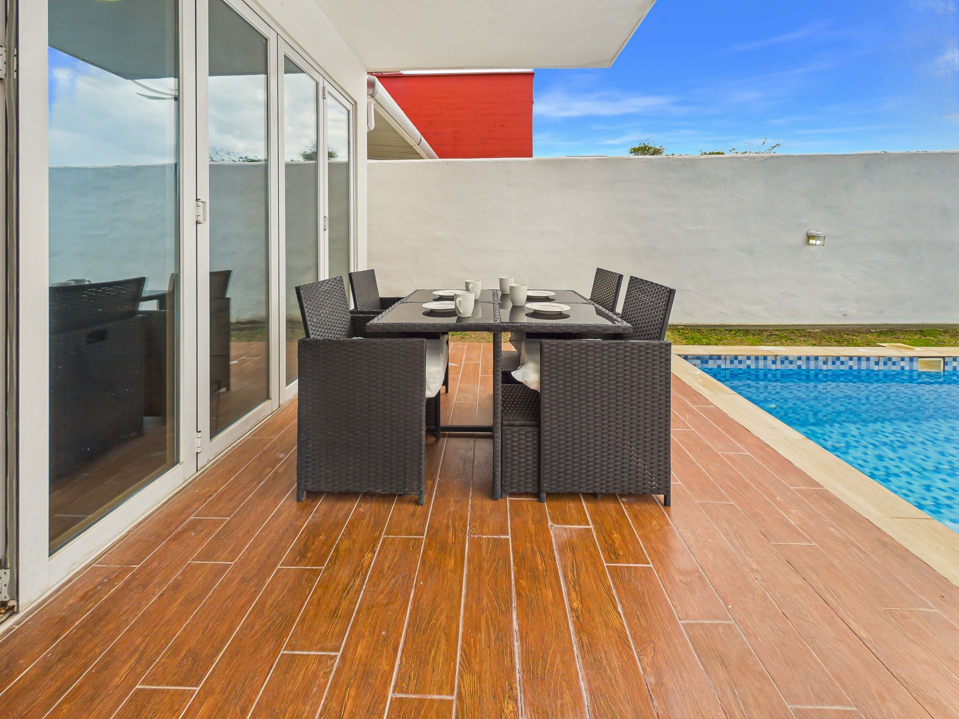 Conjunto de comedor en el patio, junto a una piscina azul, con puertas de cristal y una moderna pared de balcón.