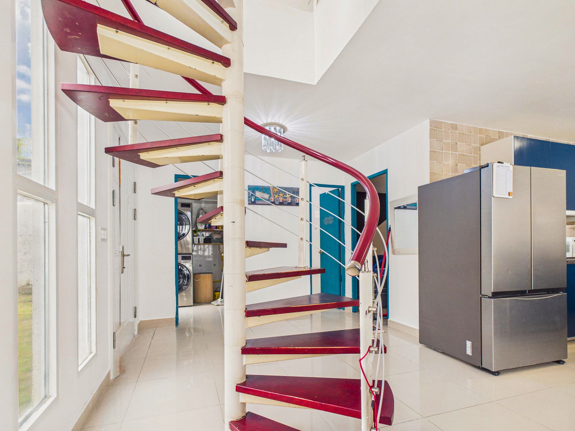 Interior de una casa moderna con una escalera de caracol roja y un refrigerador de acero inoxidable.