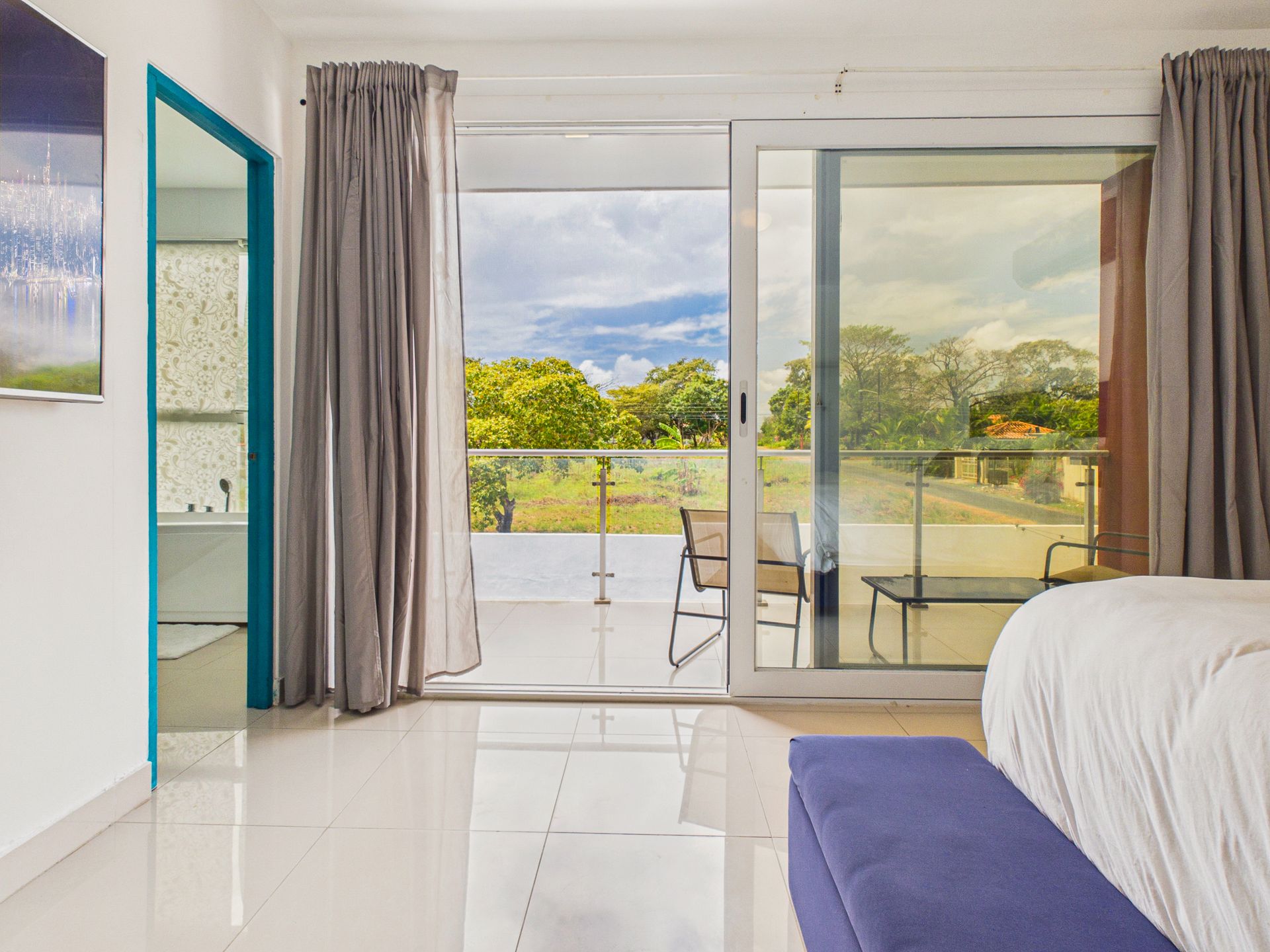 Habitación luminosa con puertas de cristal abiertas que dan a una terraza y vistas a una exuberante vegetación.