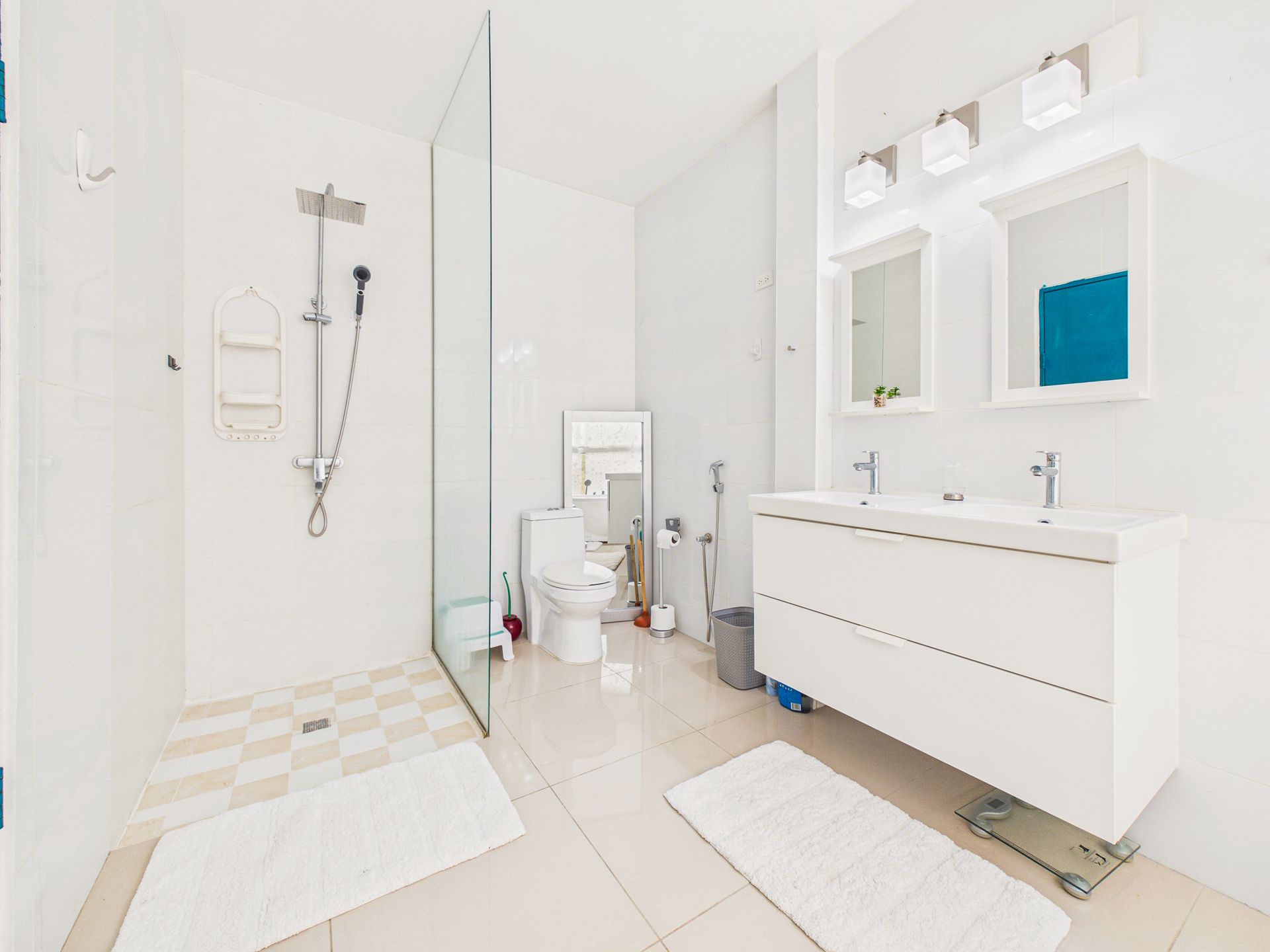 Baño moderno de color blanco brillante con ducha a ras de suelo, inodoro y tocador flotante con armarios con espejo.