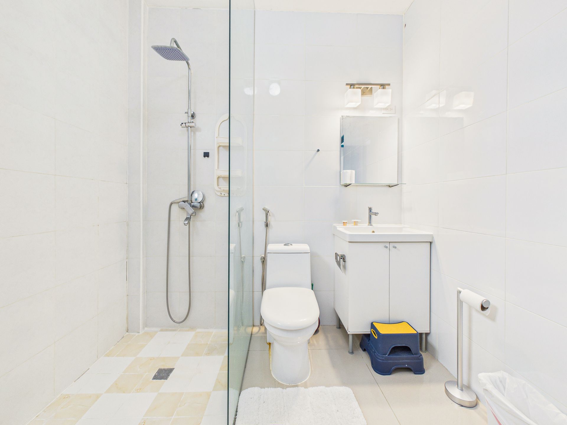 Baño moderno de color blanco con ducha a ras de suelo, inodoro, lavabo, espejo y taburete.