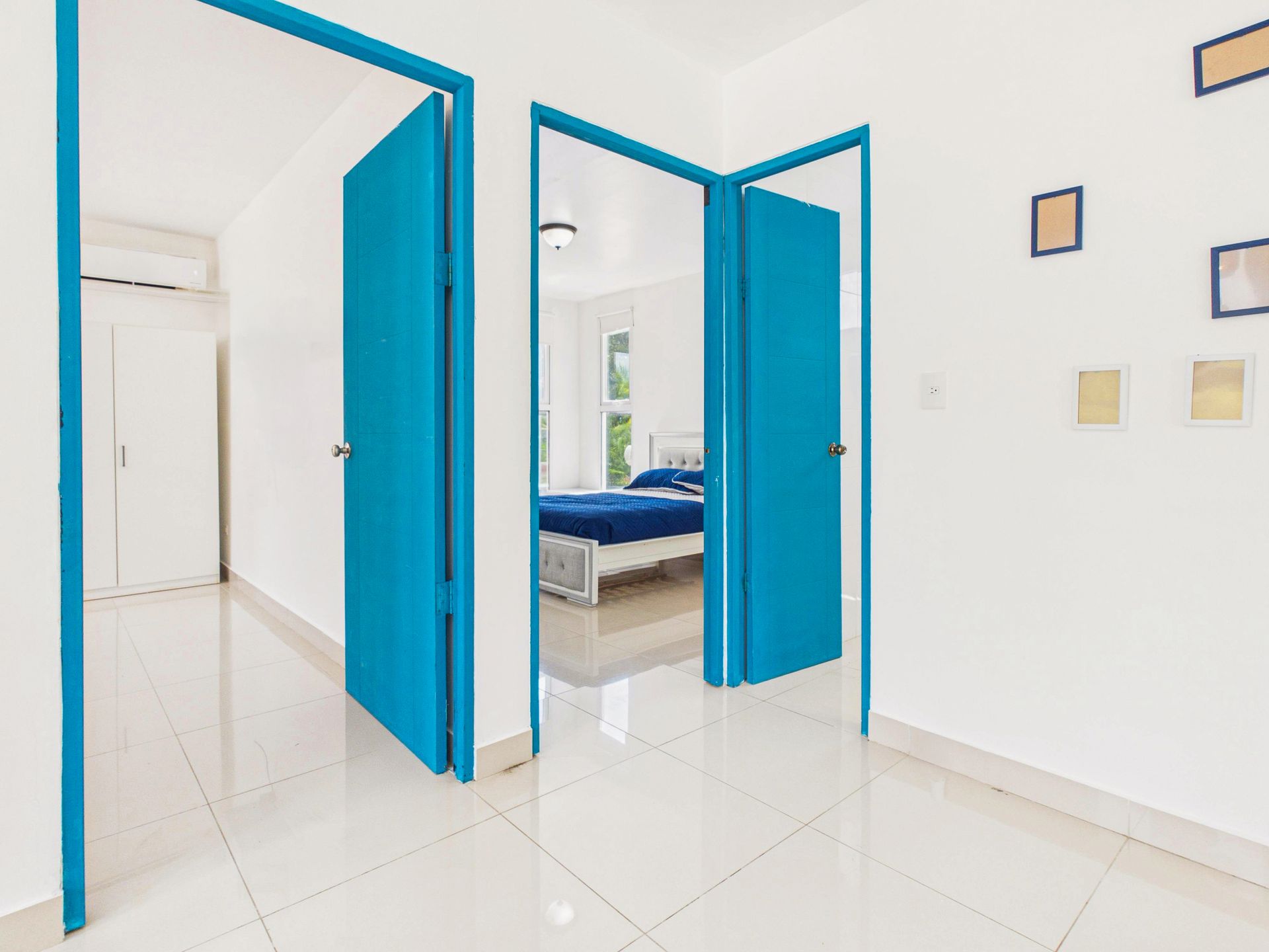 Habitación luminosa con marcos de puerta azules y suelo blanco brillante, que deja ver parte de un dormitorio.