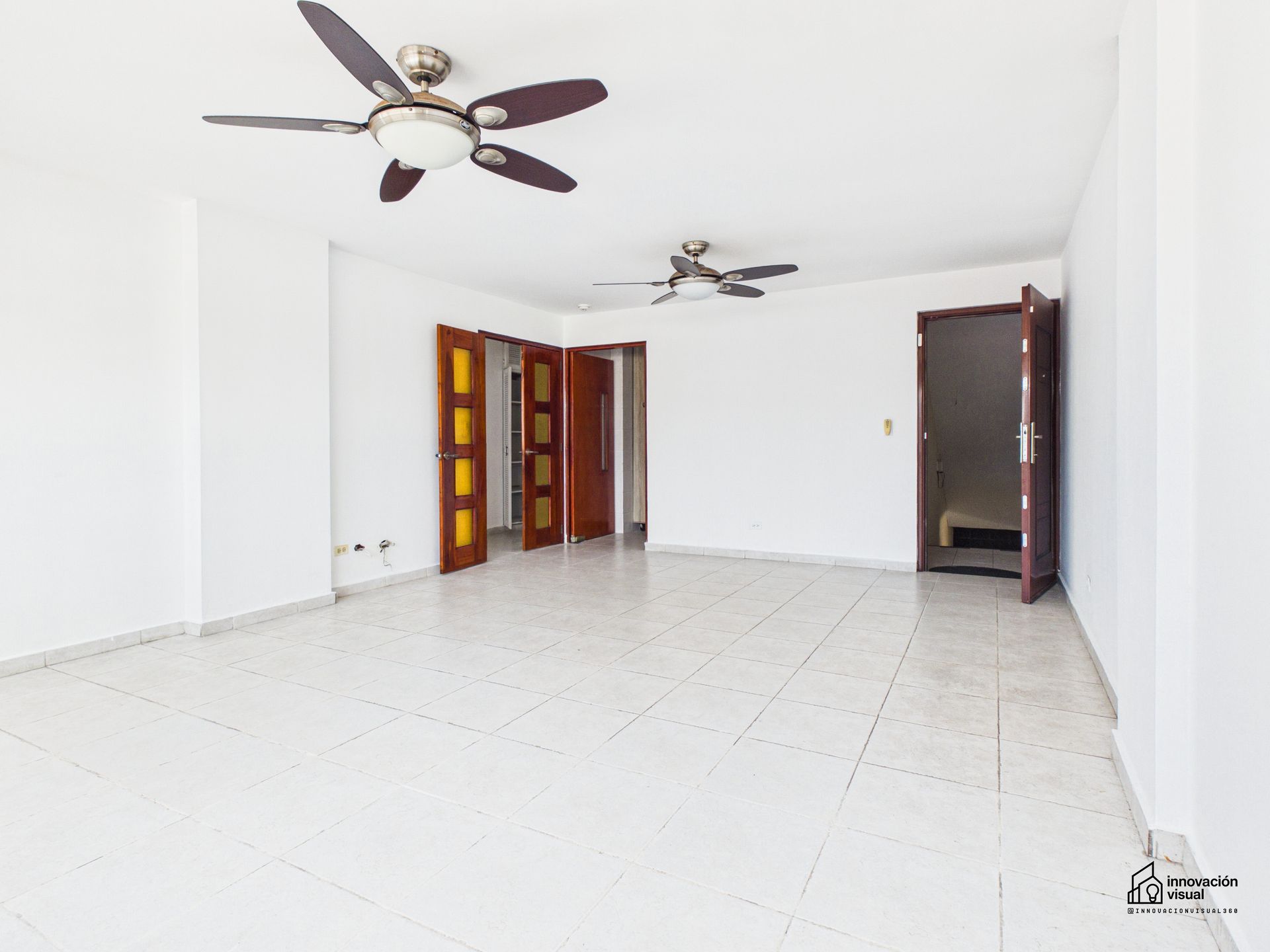 Habitación blanca vacía con suelo de baldosas, puertas marrones y ventiladores de techo.